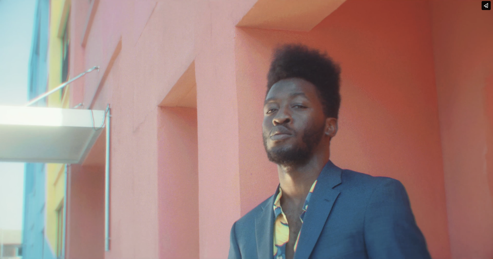 A young man standing in front of a colorful pink wall with painted panels.