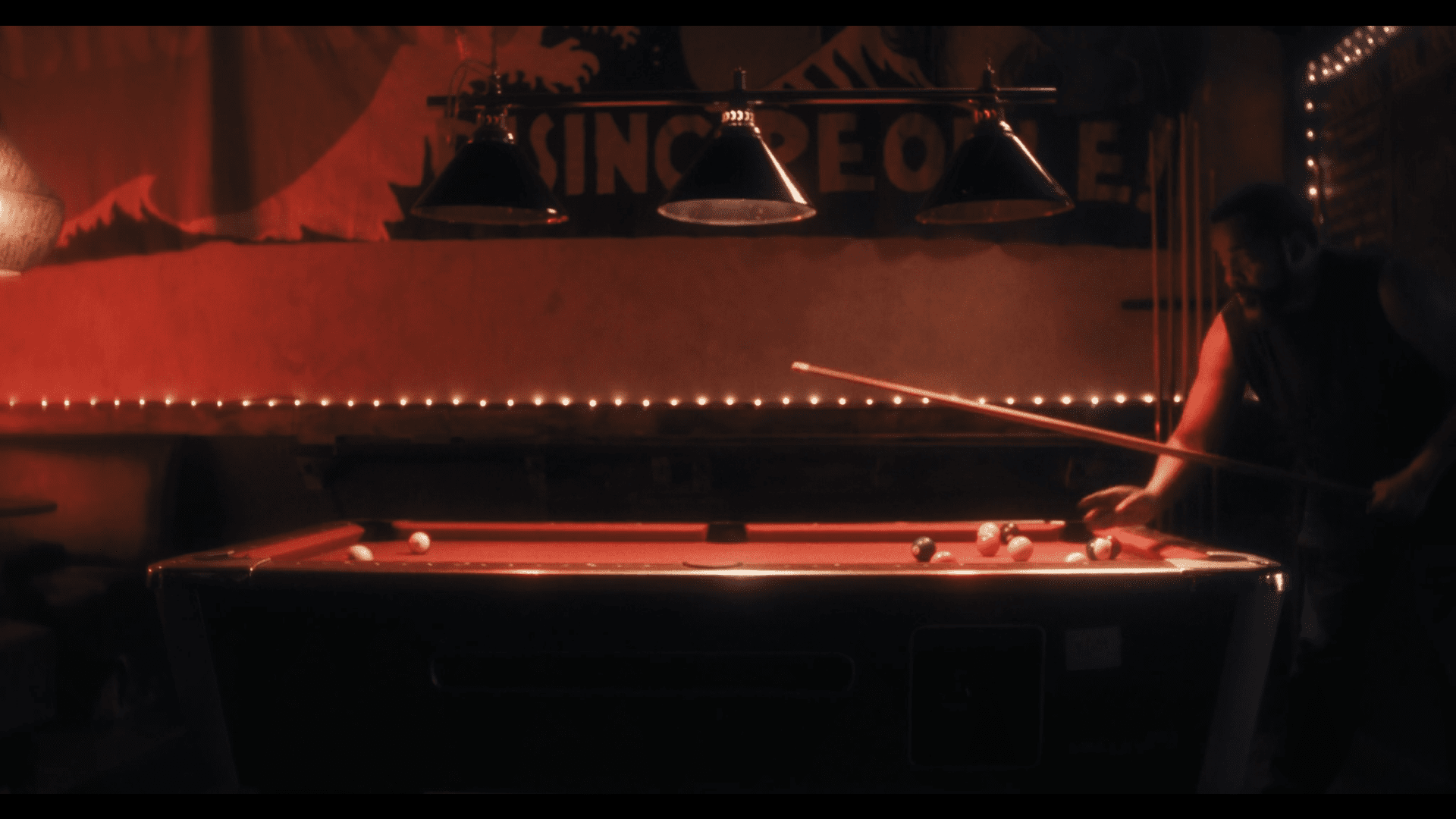 A man playing pool under dim red and orange lighting in a bar or pool hall.