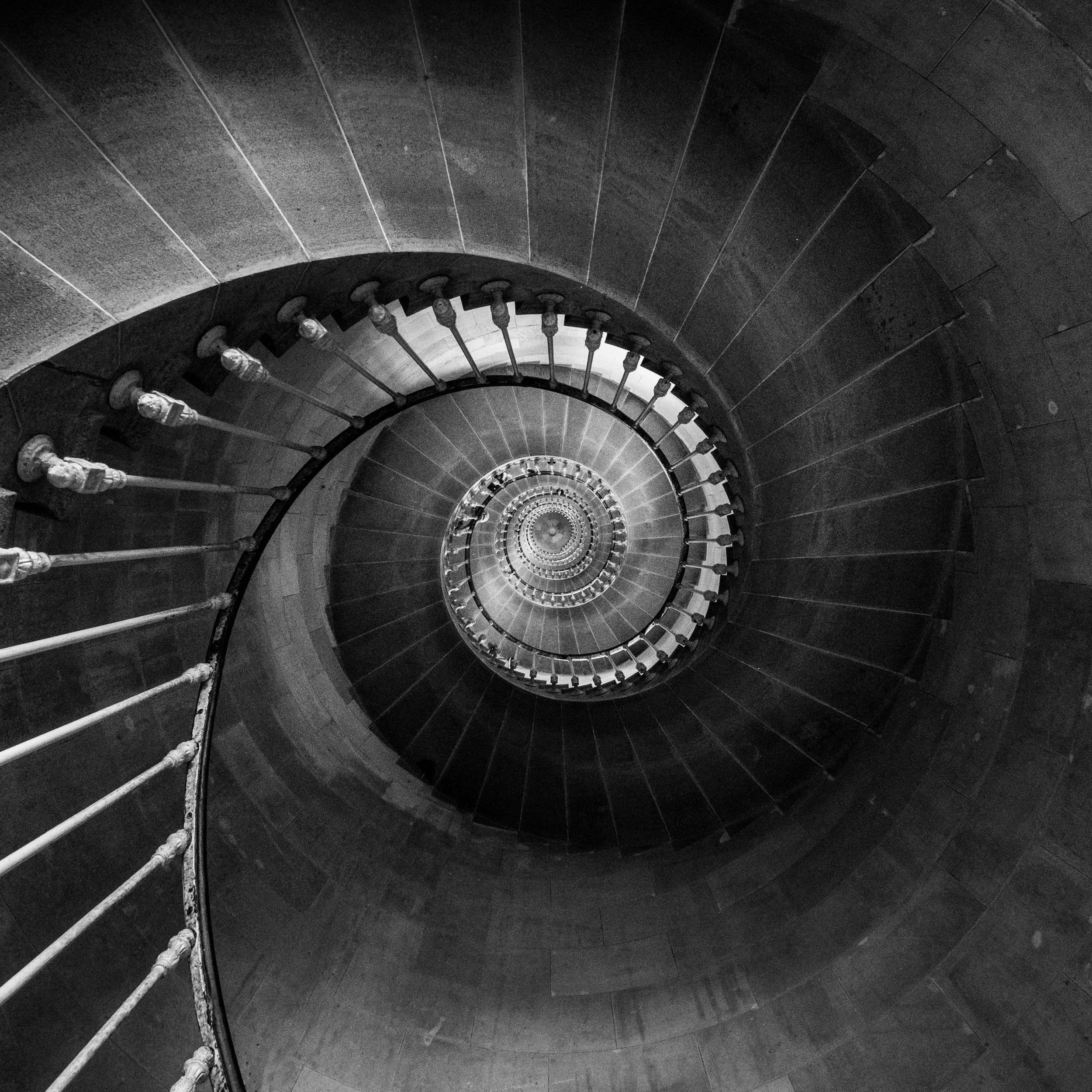 Spiral staircase viewed from above, showing steps and handrails winding downward.