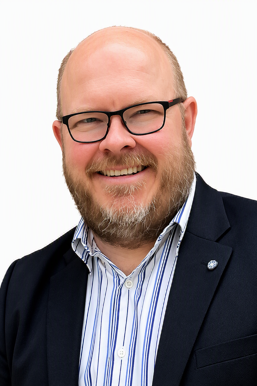 A smiling man with glasses, a beard, and a bald head, wearing a dark blazer over a striped shirt, against a white background.