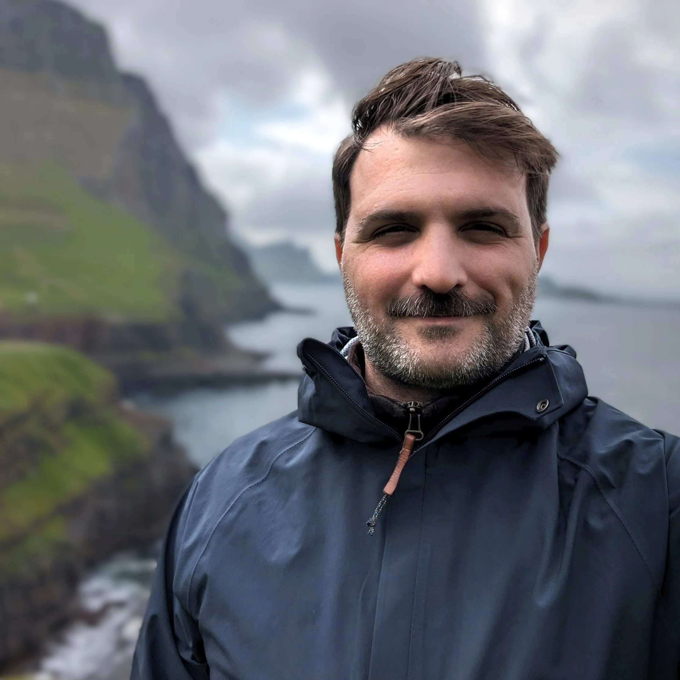 Mark Franklin. A man with short brown hair and a beard smiling outdoors on a cloudy day, wearing a dark jacket.
