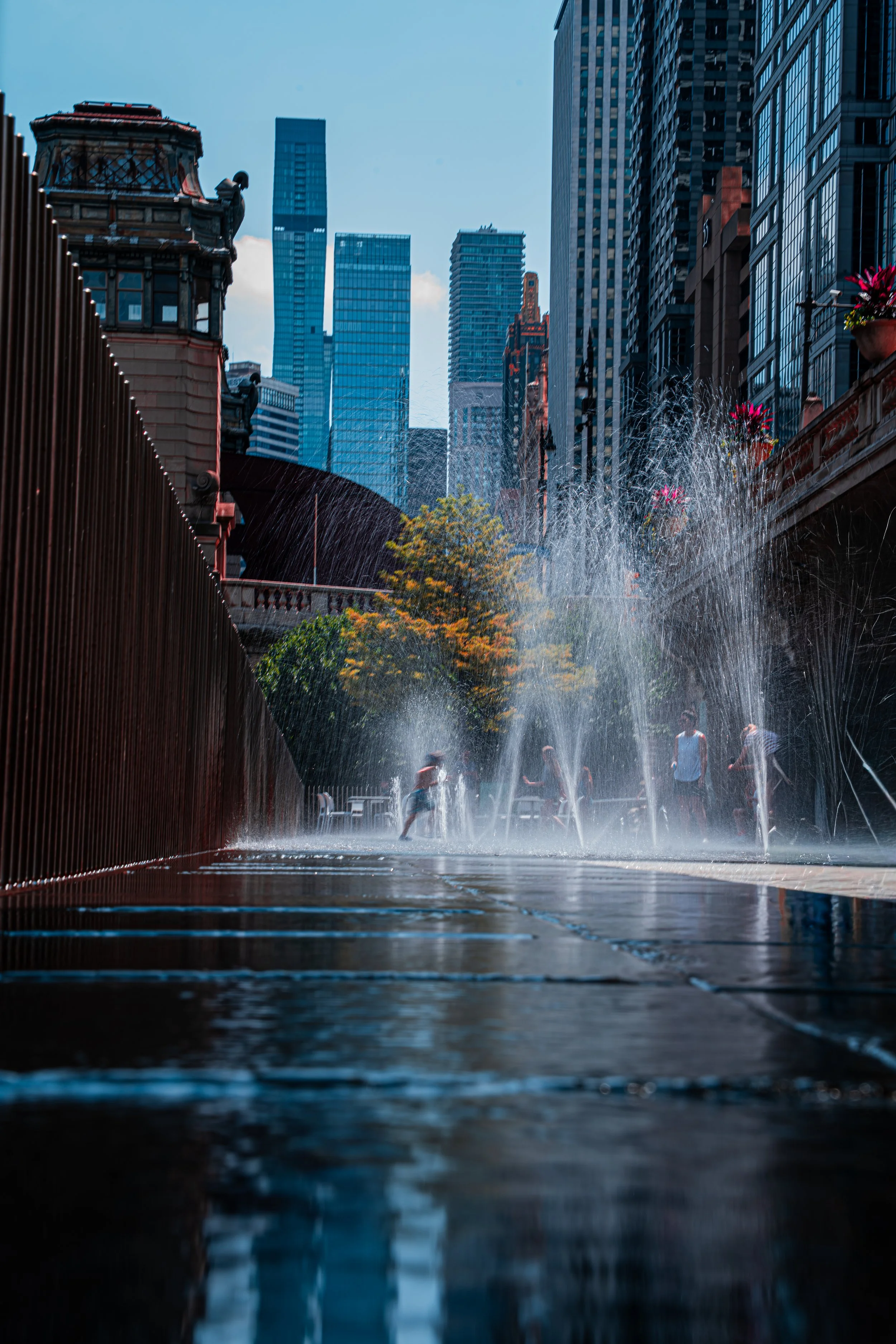 People walking through a water fountain in a city with tall skyscrapers and modern buildings in the background.