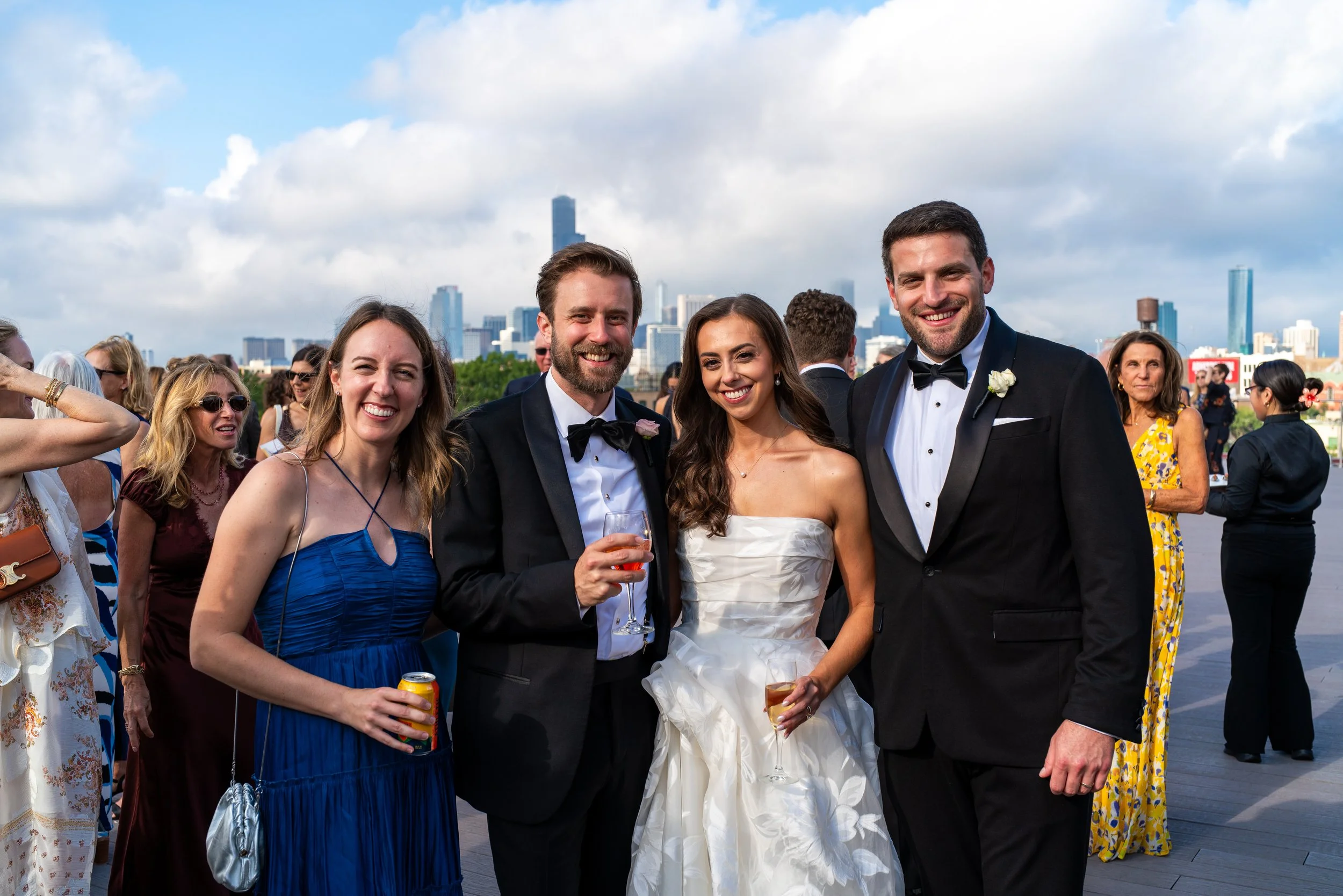 Group of people dressed in formal attire at an outdoor event with a city skyline in the background.