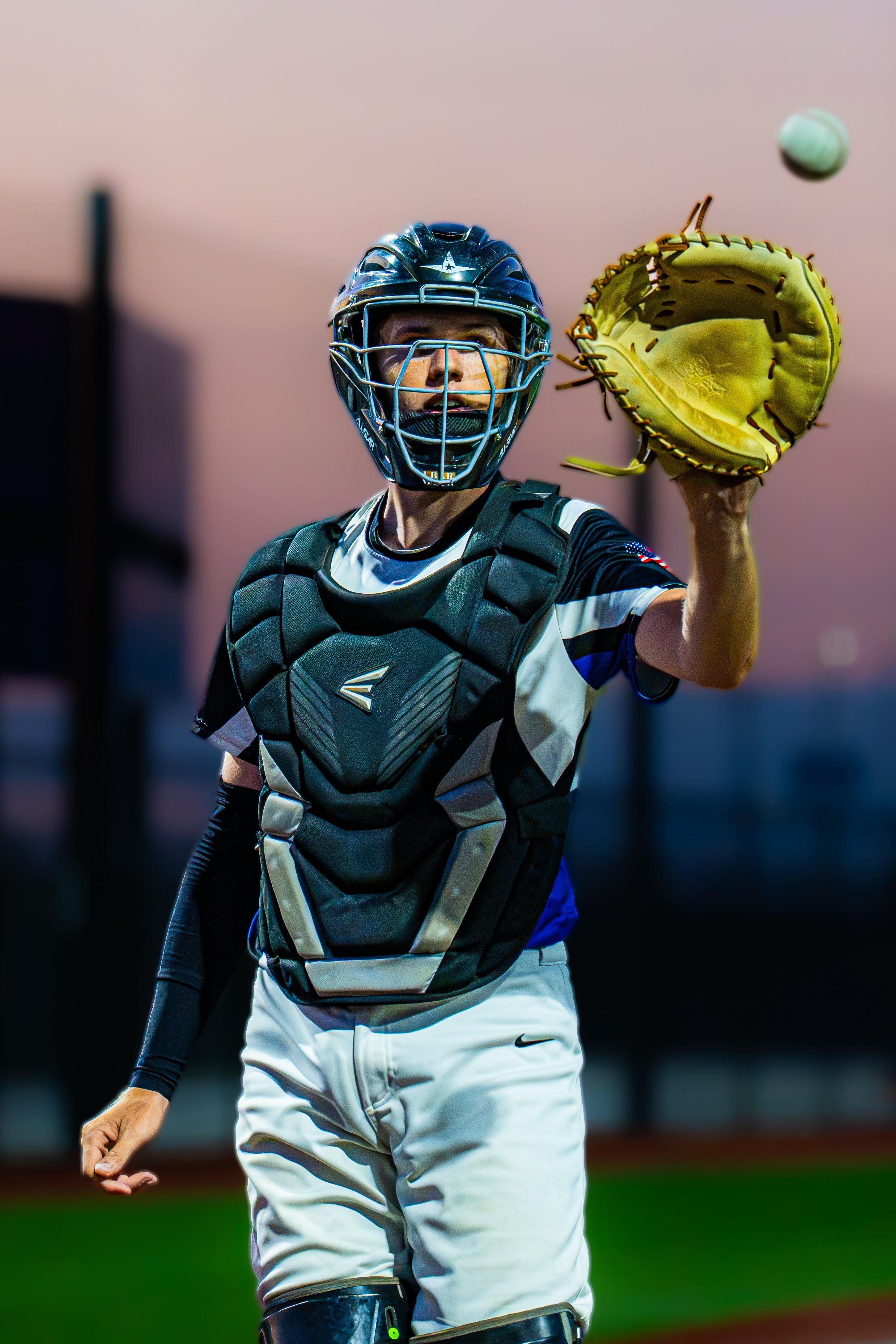 A baseball catcher in uniform and protective gear catching a baseball with his mitt during a game.