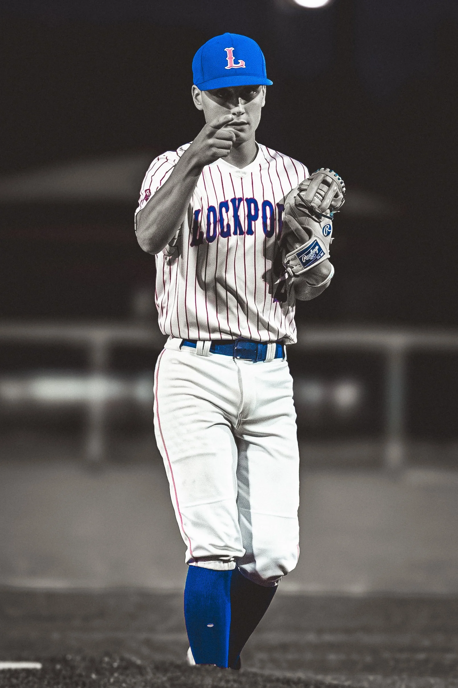 A baseball player in uniform standing on a baseball field. The image is black and white except for the player's hat, shirt, and socks, which are blue and red.