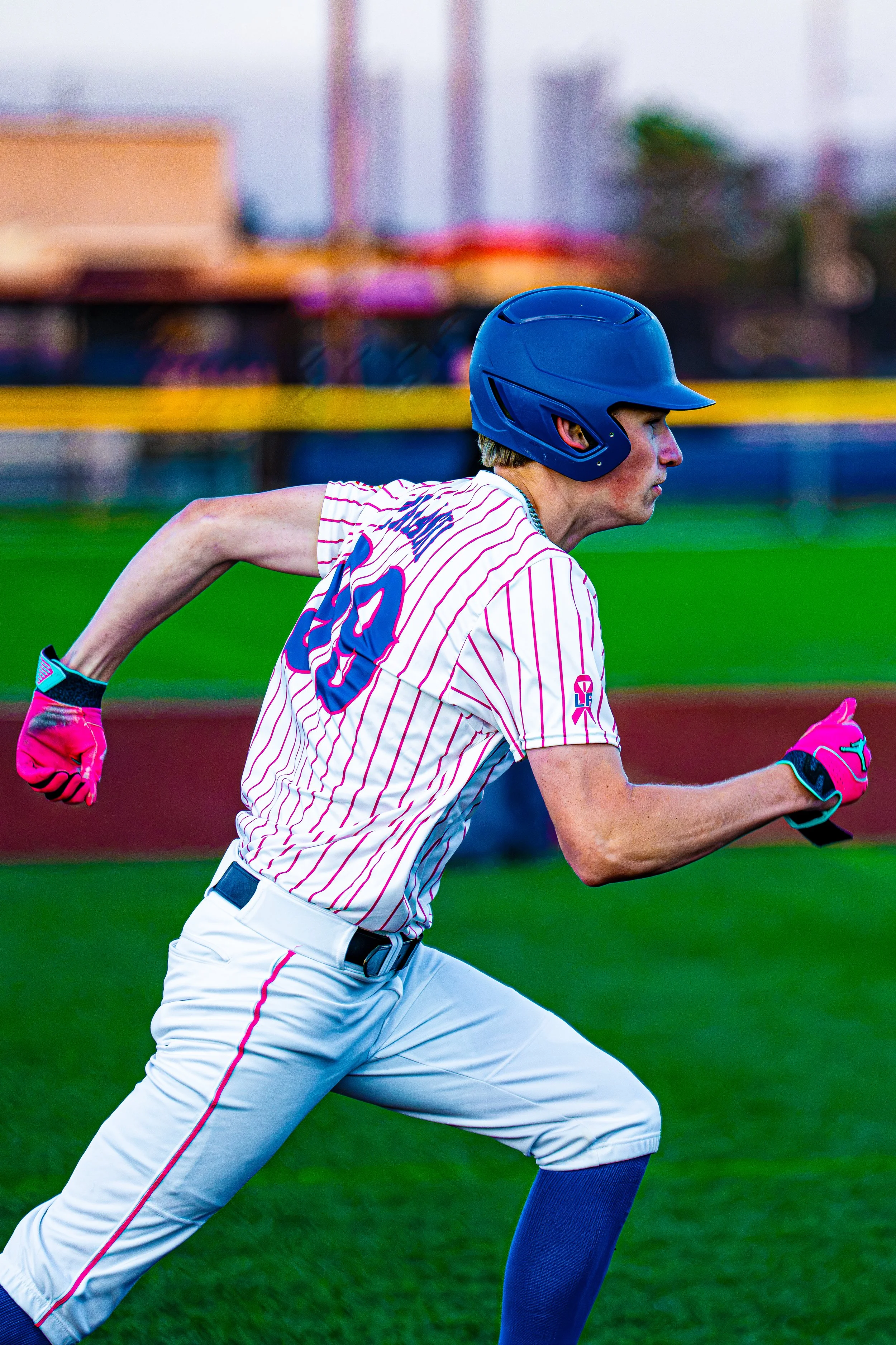 A baseball player in a white uniform with pink stripes and a blue helmet running on the field during a game.