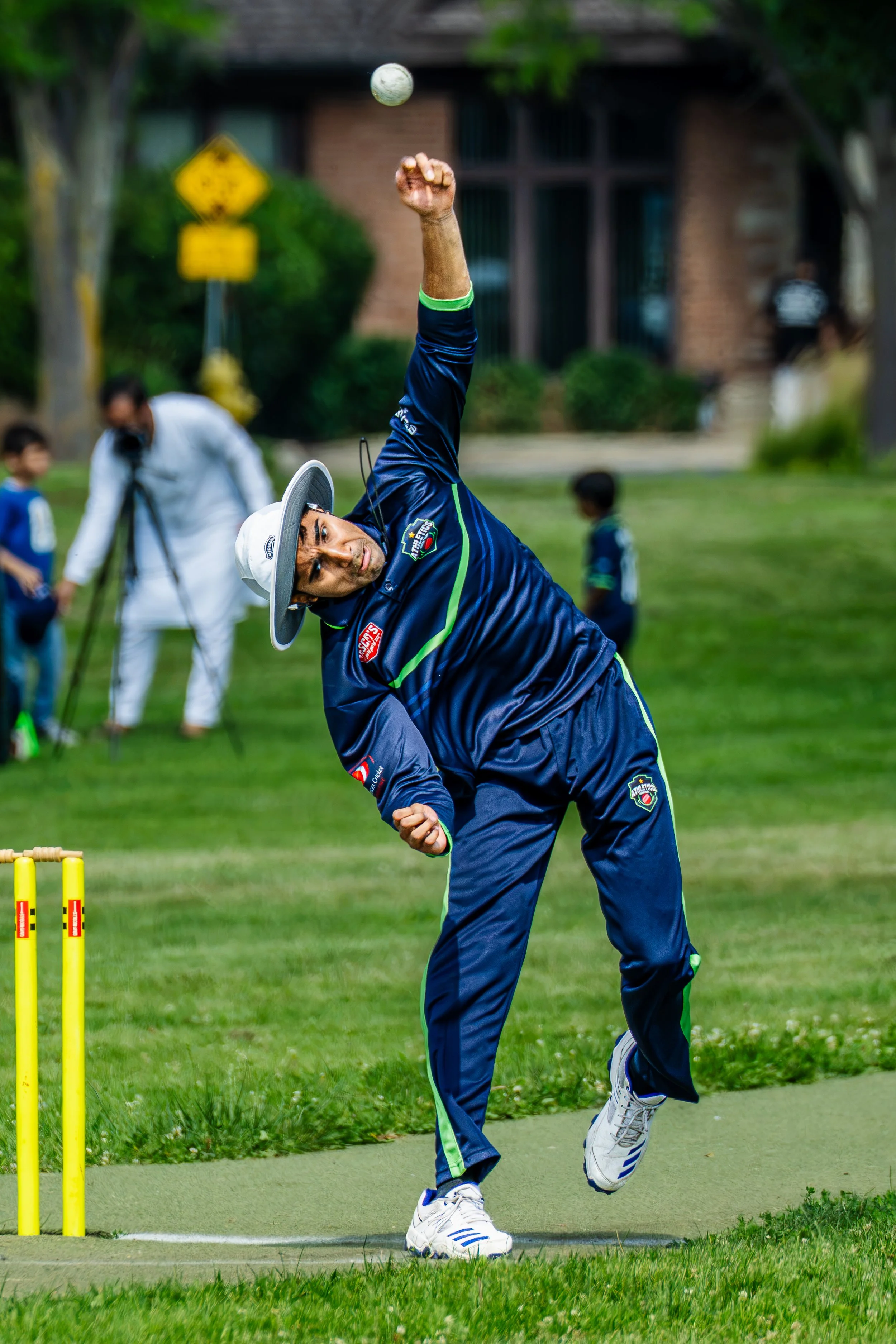 A man playing cricket, about to hit a ball with a cricket bat, on a grassy field with wickets nearby.