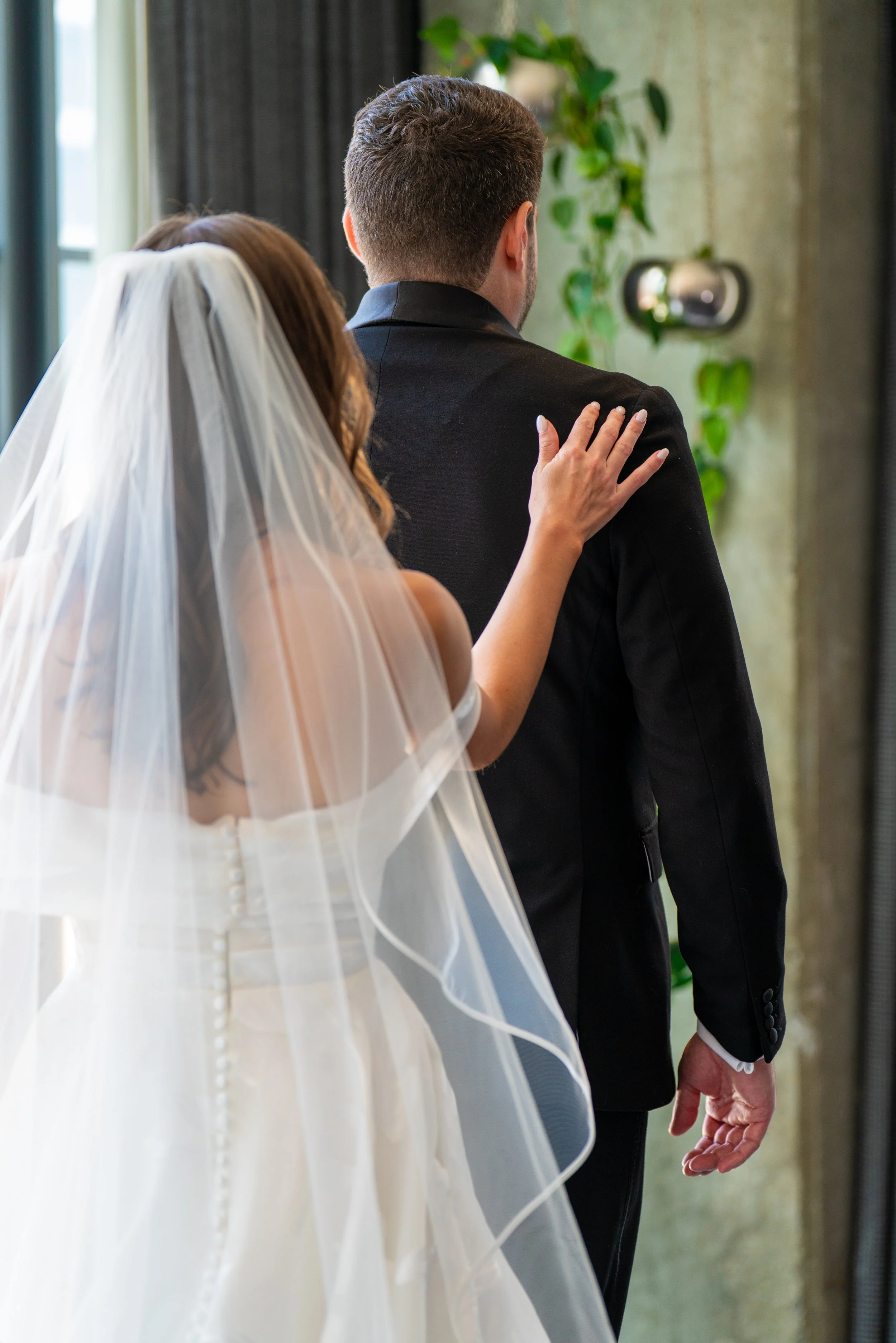 A bride and groom stand side by side during a wedding ceremony, with the bride gently touching the groom's shoulder.