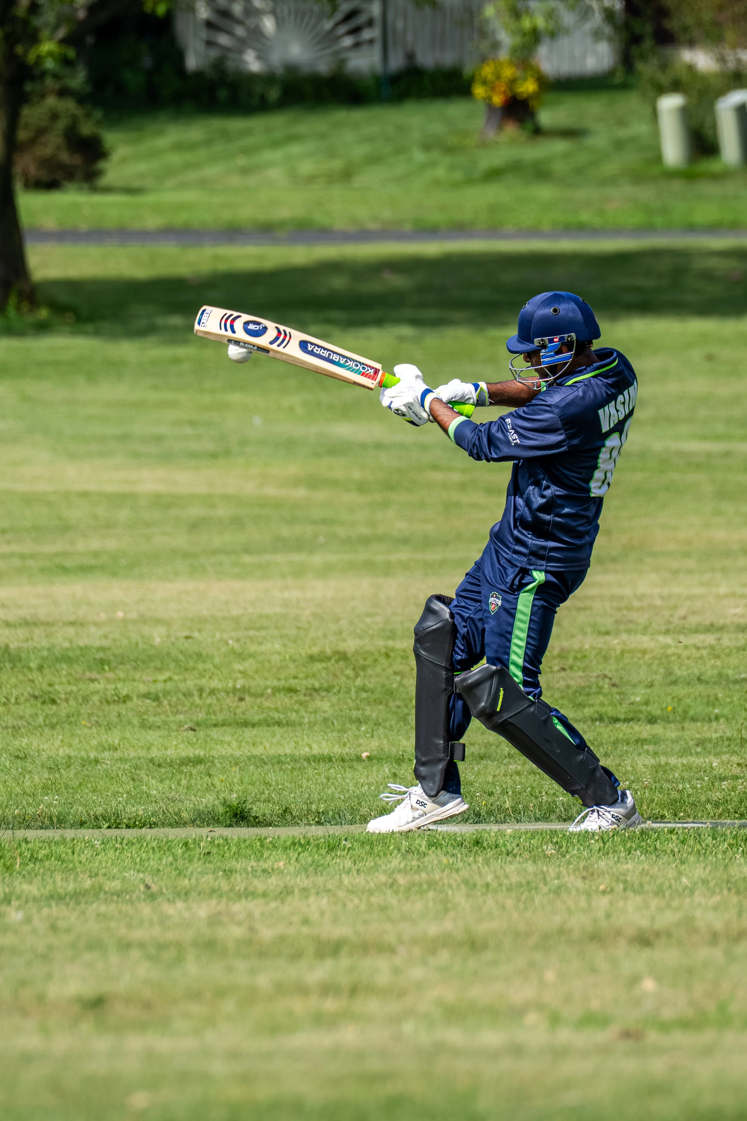 A cricket player in blue uniform and helmet hitting a ball with a cricket bat on a green field.
