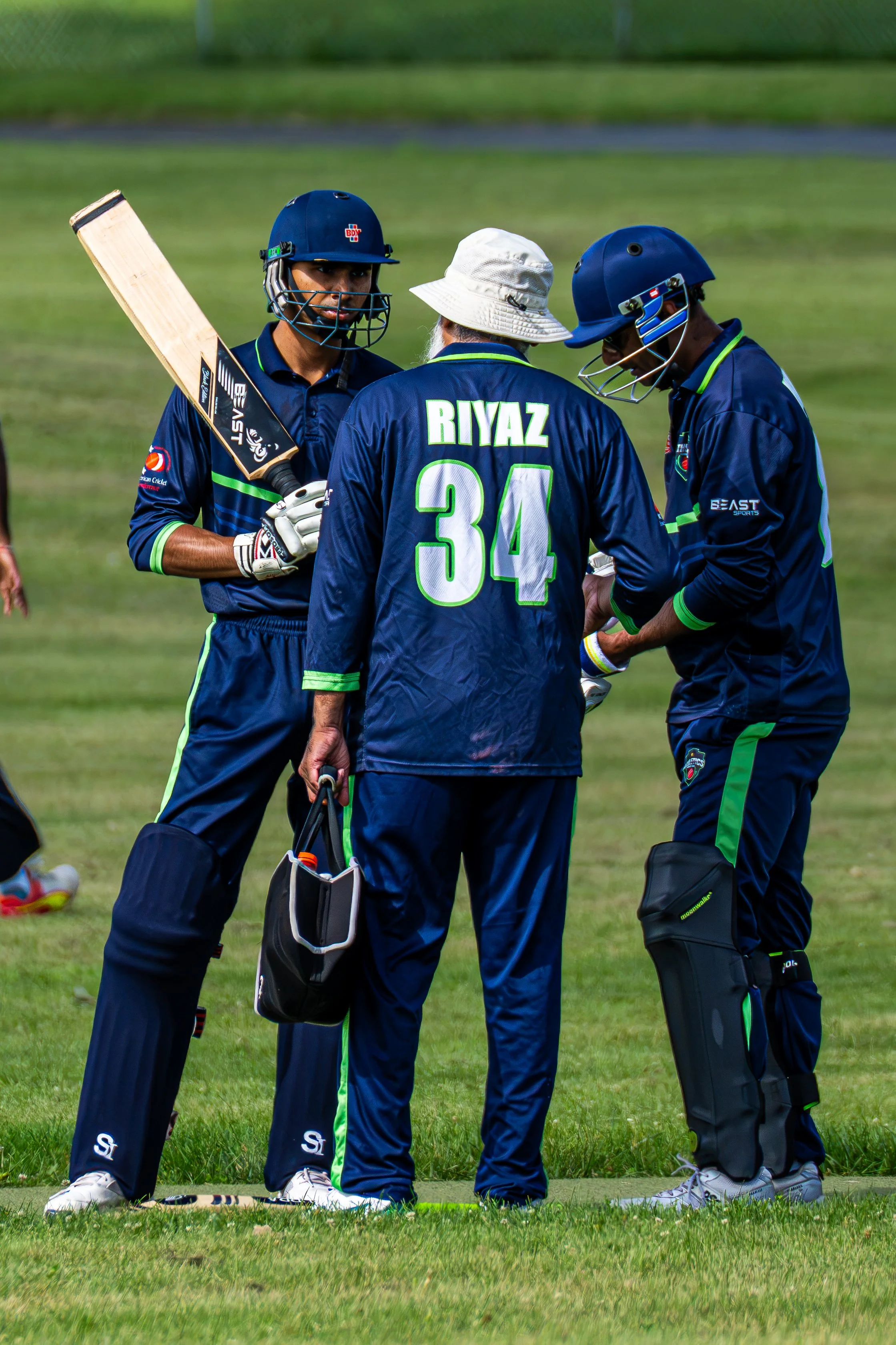 Two cricket players and a coach or umpire in discussion on a grassy field.