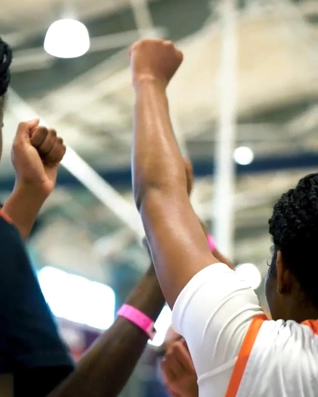 Multiple people raising their fists in a gesture of solidarity or protest, indoors with blurred background.