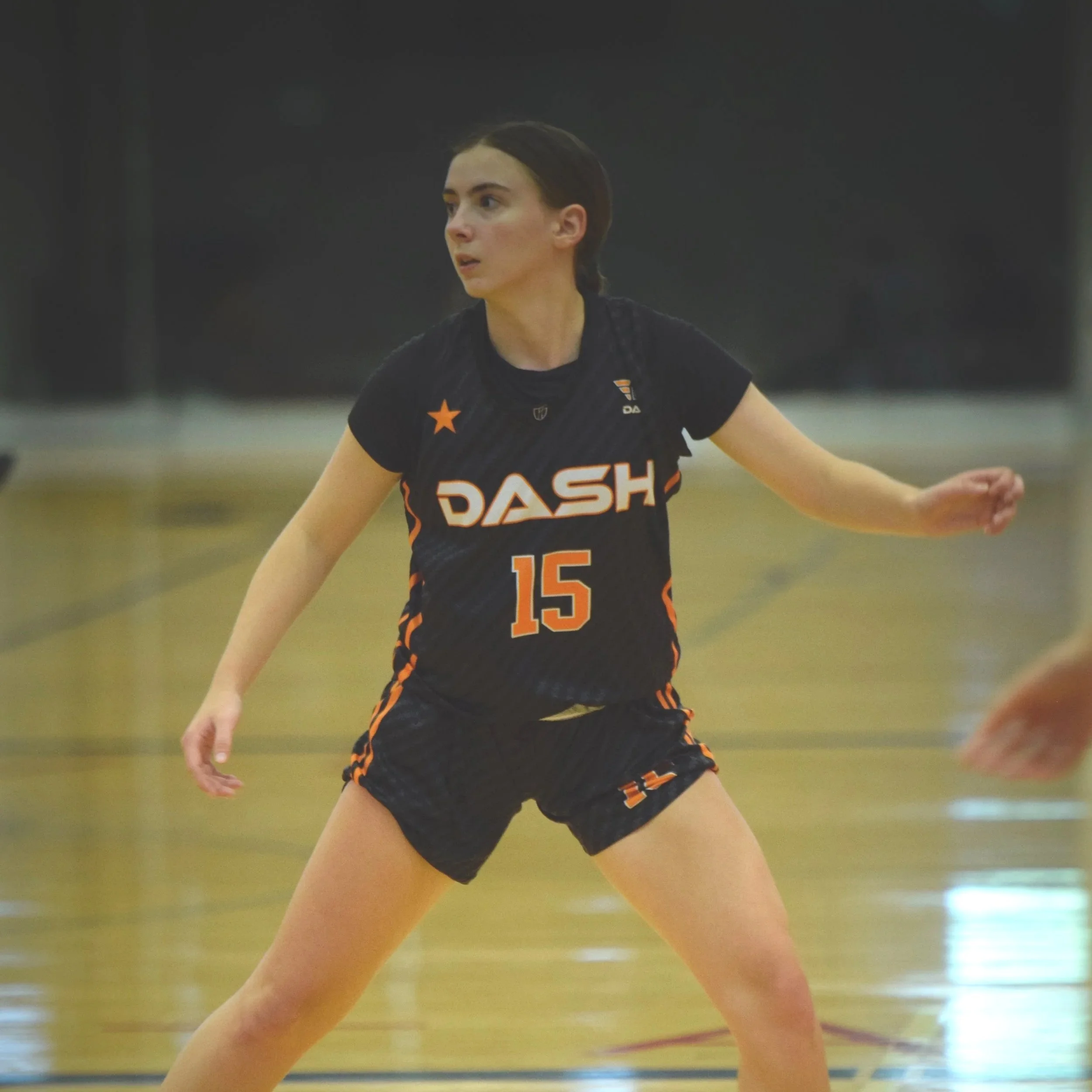A female athlete in black sportswear, with the word DASH on her shirt and the number 15, is playing volleyball on an indoor court.