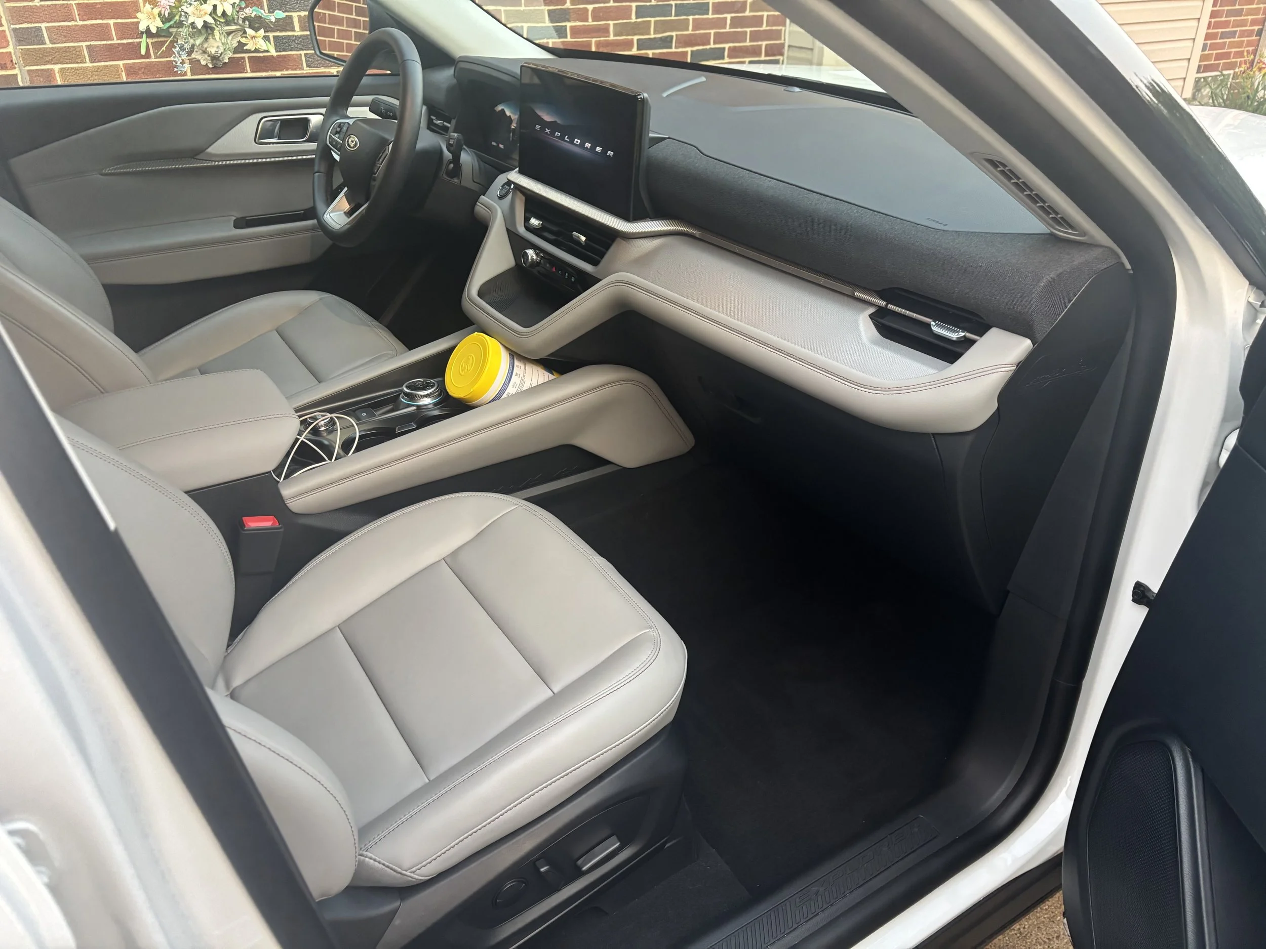 The interior of a modern vehicle showing beige leather seats, a dashboard with a digital display, and a steering wheel with the Ford logo. There is a yellow container and a pair of earphones on the center console.