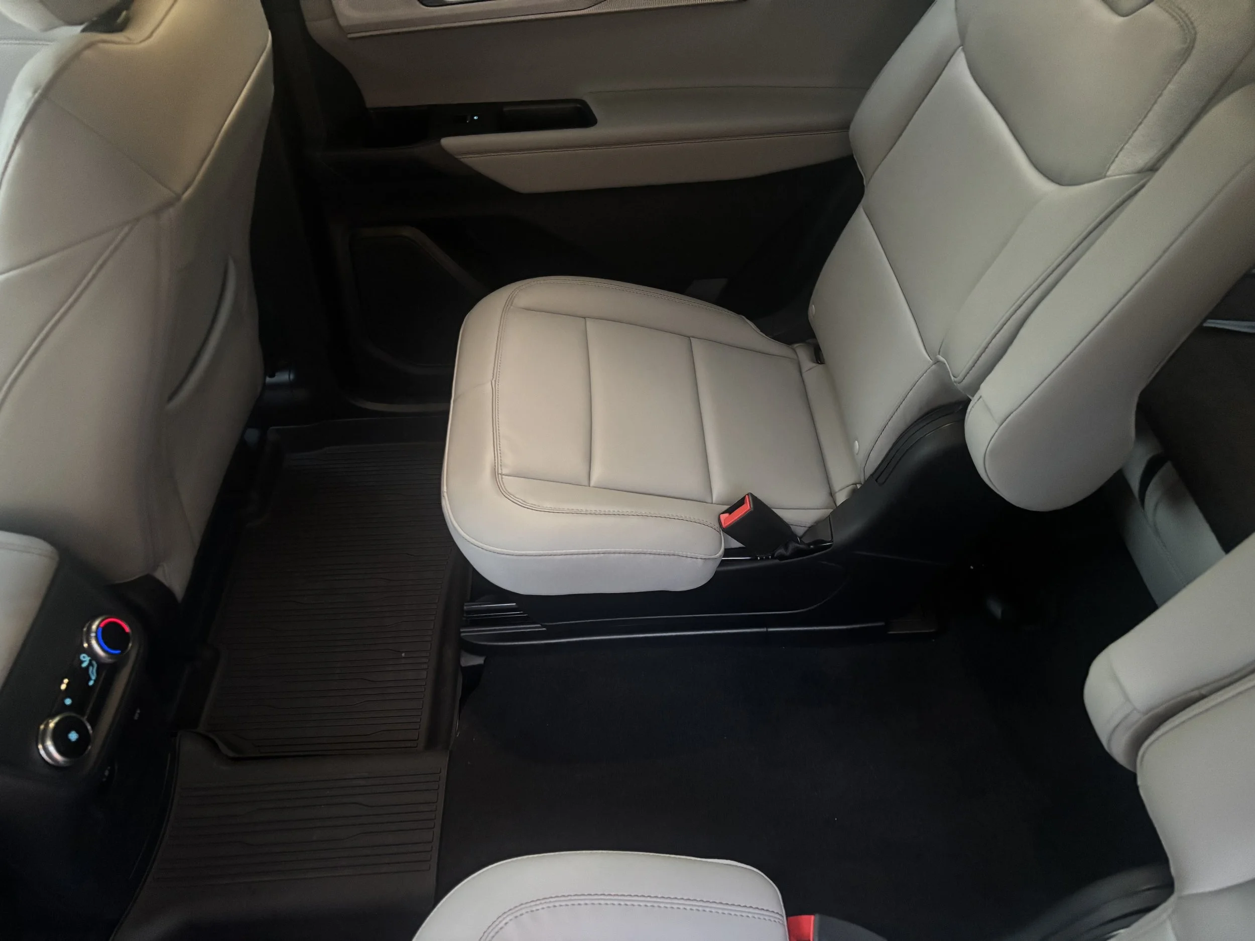 The interior of a car showing the back seats with beige upholstery, part of the front passenger seat, and a black center console with climate controls.