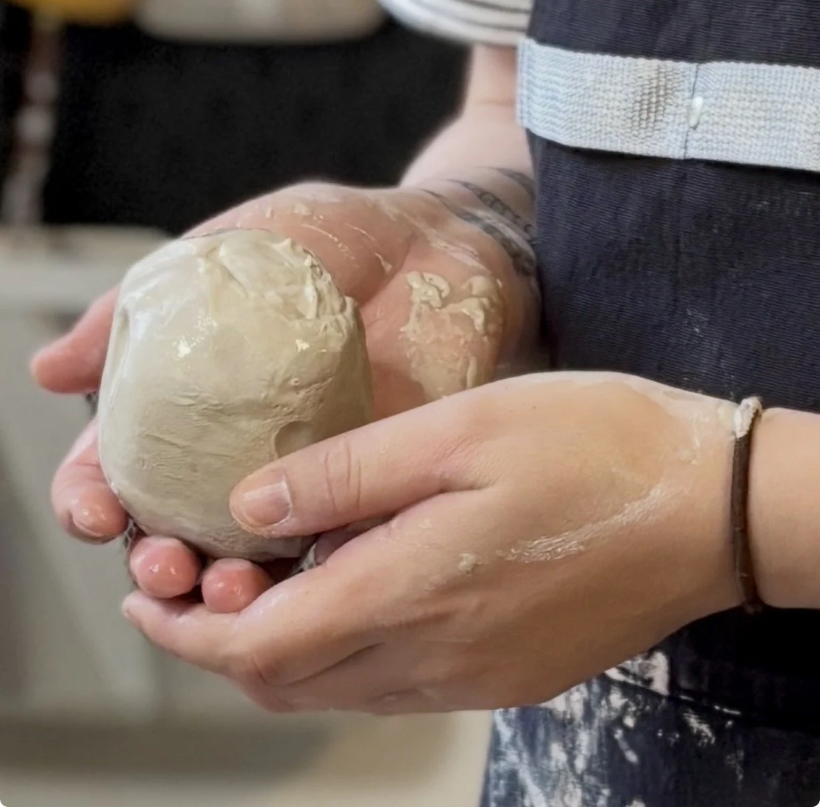 Person holding a ball of clay with their hands covered in wet clay.