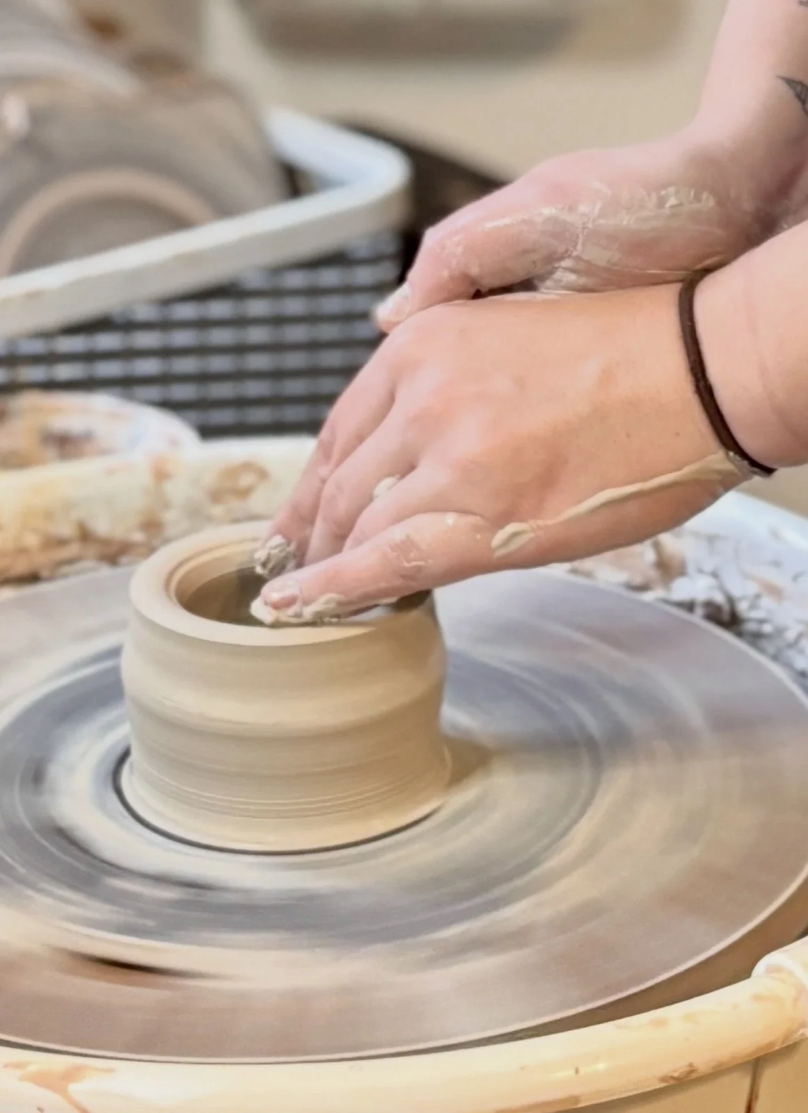 Close-up of a person's hands shaping a clay pot on a pottery wheel in a ceramics studio.