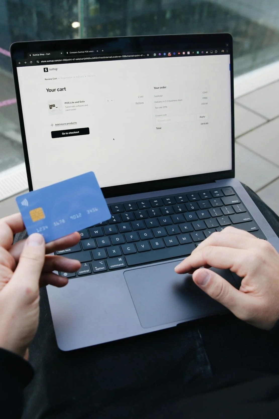A person holding a blue credit card in front of a laptop displaying an online shopping cart checkout page