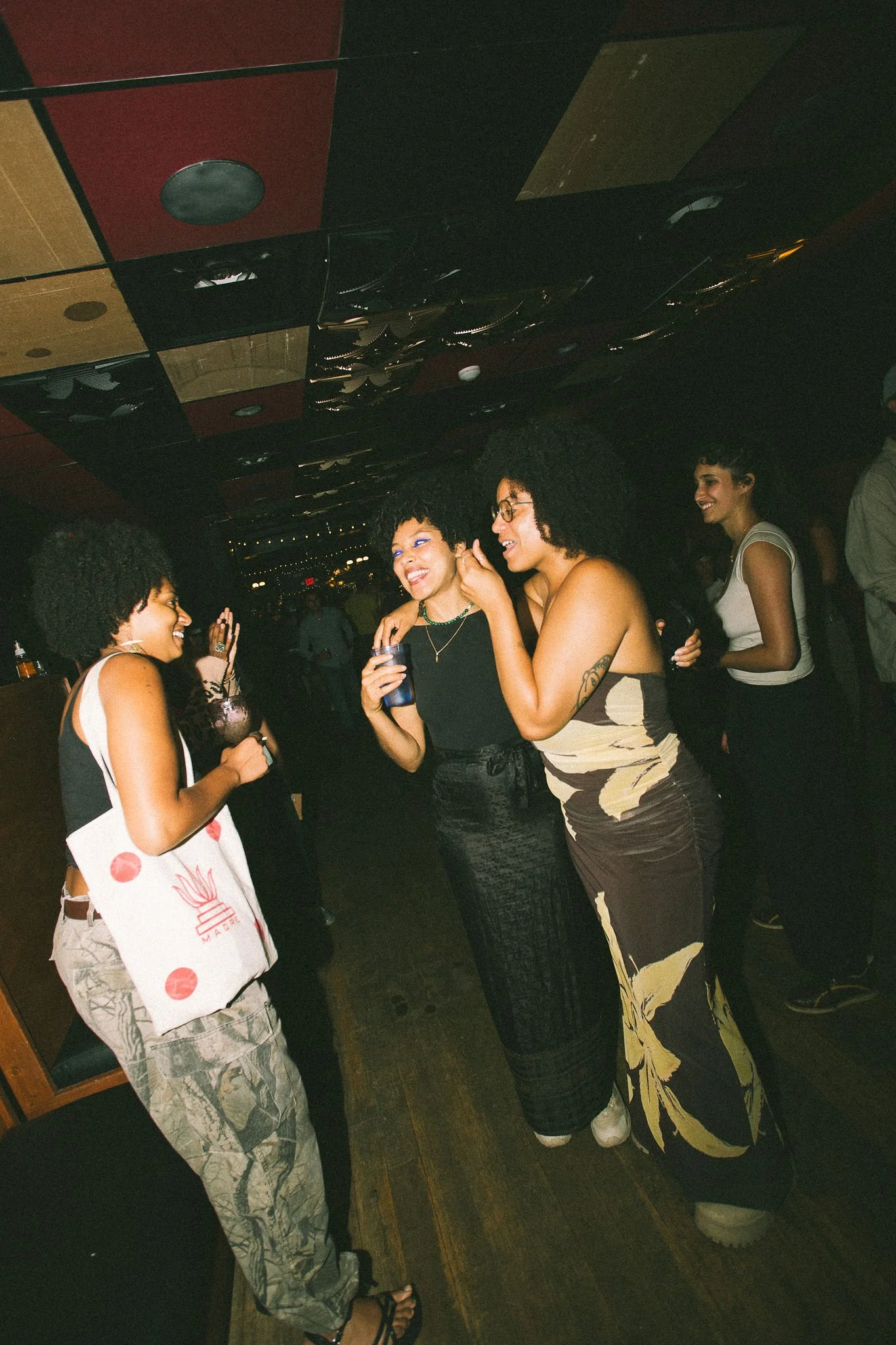 A group of women socializing and smiling in a dimly lit indoor setting, a bar or nightclub.