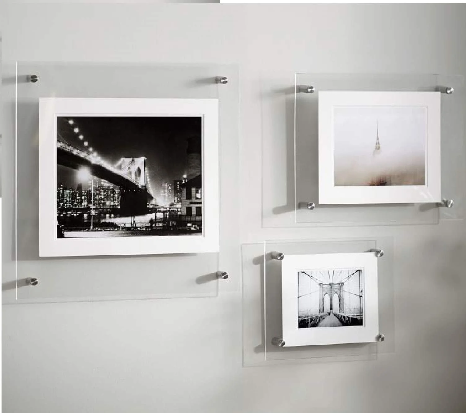 Three framed black and white photographs on a white wall, showcasing a cityscape at night, a minimal interior with a hanging light fixture, and a bridge.