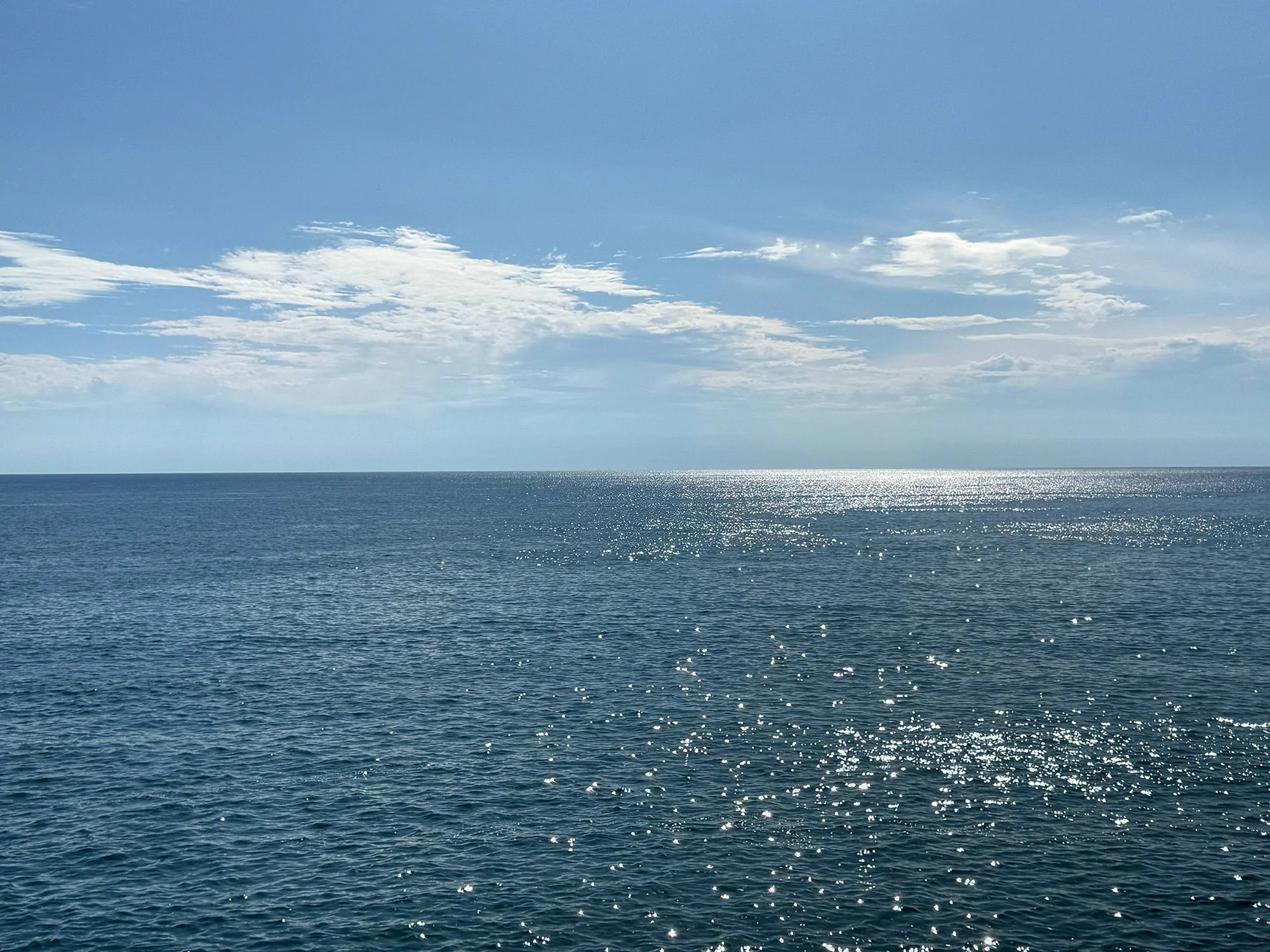 Open ocean with a reflection of sunlight on the water, partially cloudy sky.
