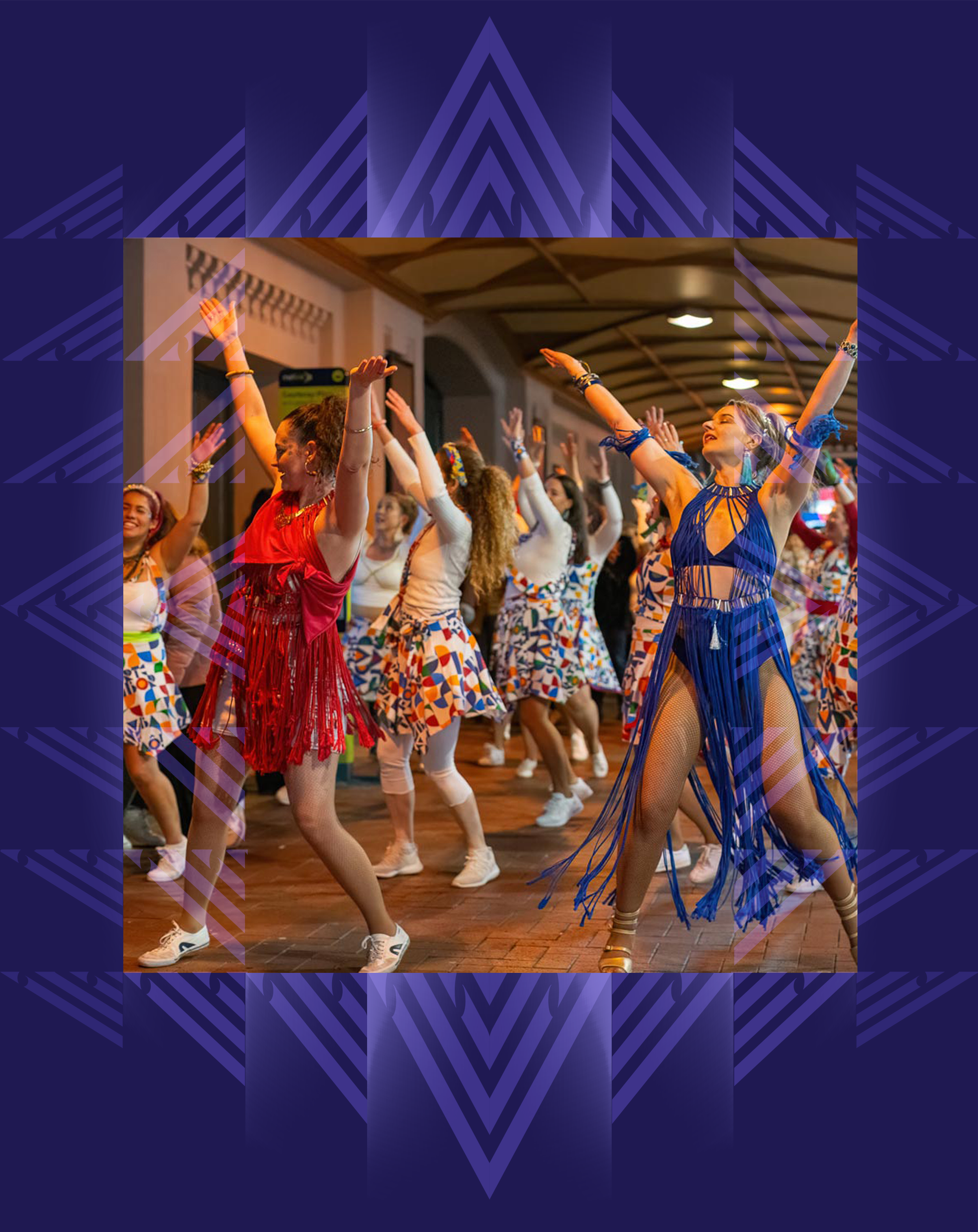 Group of women dancing in colorful outfits and accessories at an indoor event, with a wooden ceiling and warm lighting.