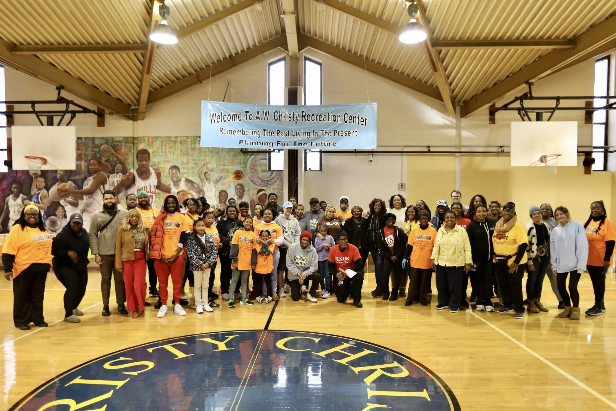 Group of people gathered in a gymnasium for a community event at A.W. Christy Recreation Center, with a banner displaying the center's name in the background.