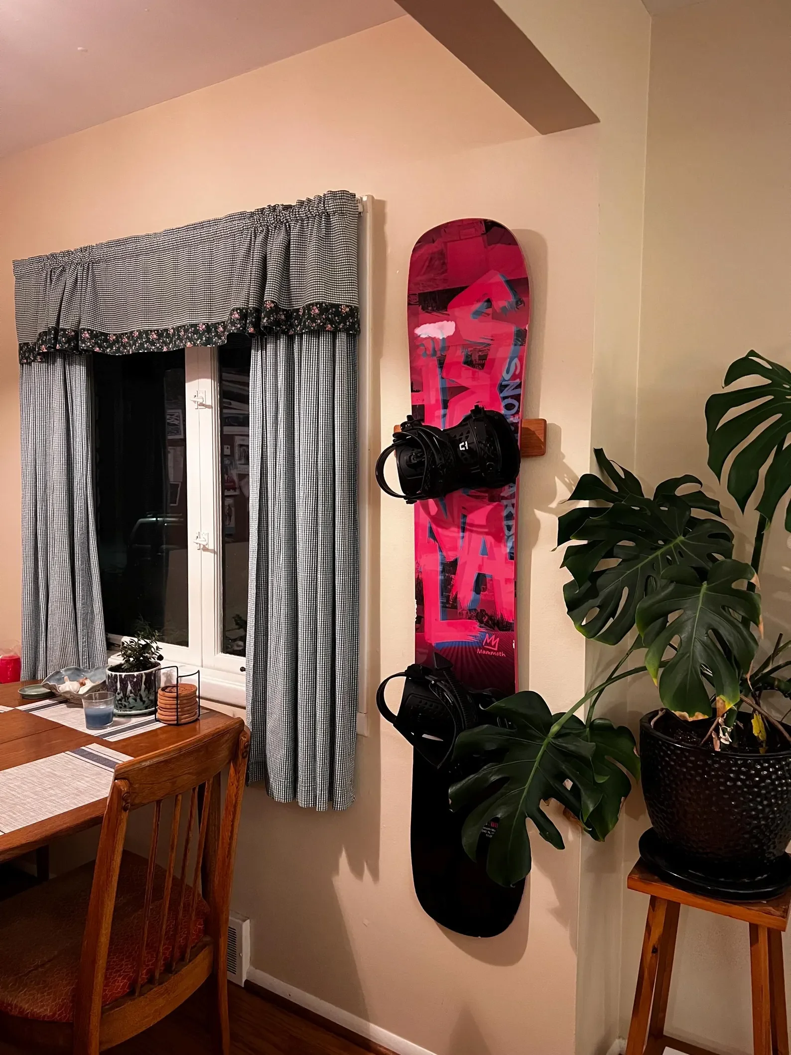 A pink Signal brand snowboard hanging from a Method Mount™ next to a large monstera and a kitchen table.