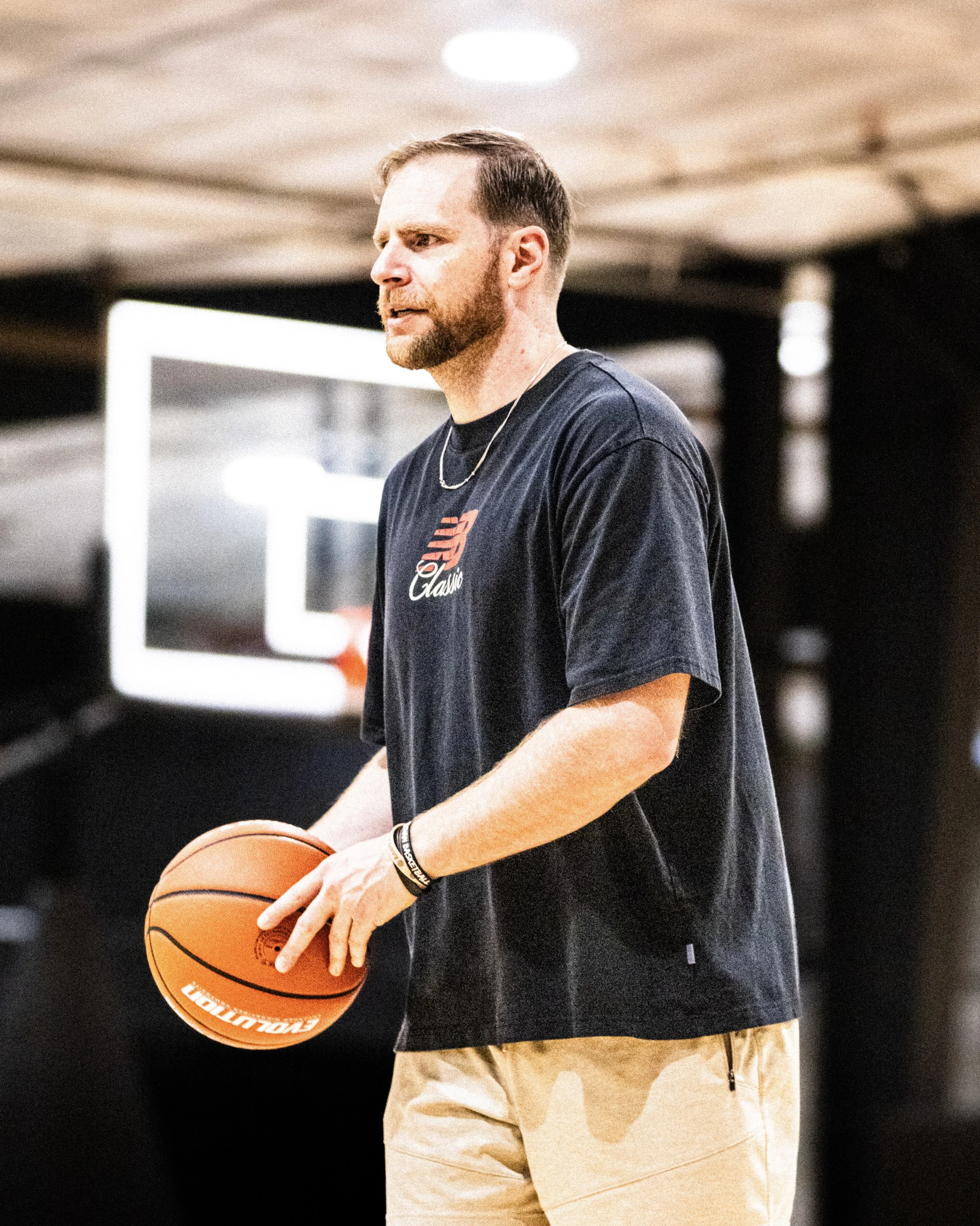 A young man with a beard holding a basketball at an indoor court.