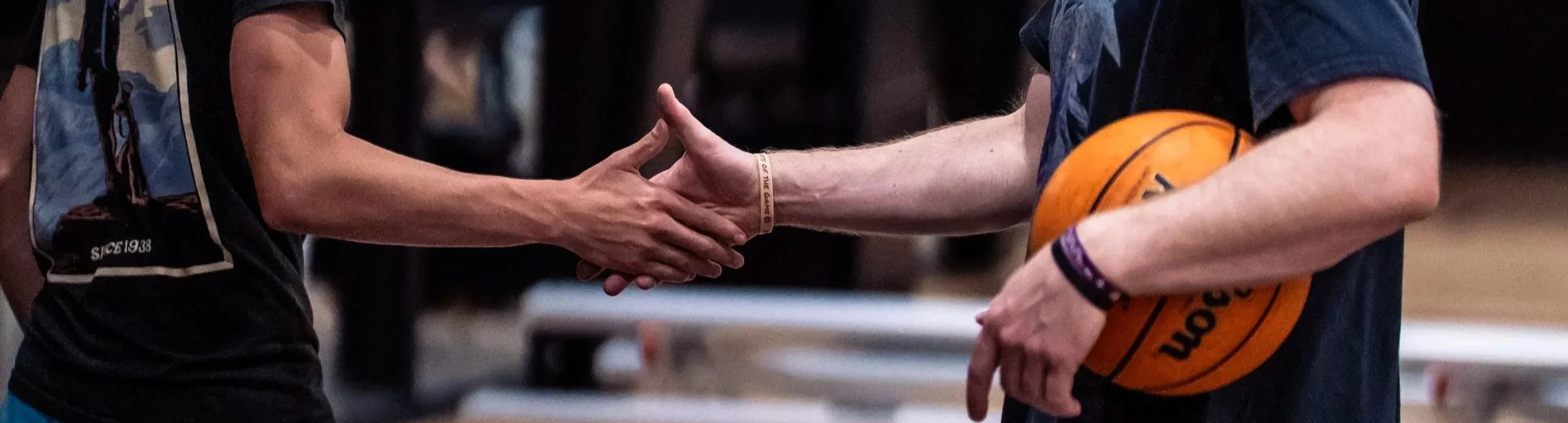 Two people are shaking hands; one person is holding a basketball, and the other person is wearing a wristband.