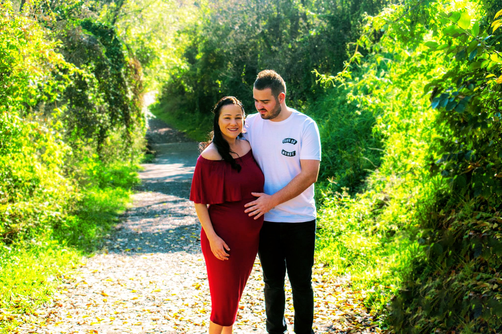 A woman smiling and a man holding her pregnant belly along a path.