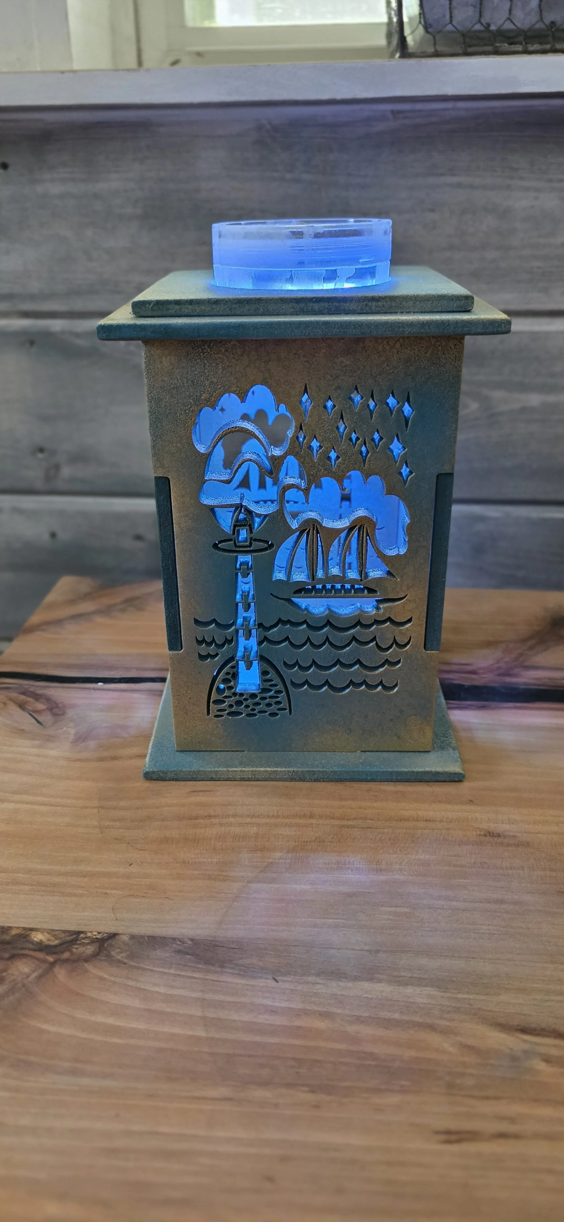 A decorative 3D lantern with a seaside scene, including a lighthouse, sailboat, clouds, stars, and water, illuminated with blue light.