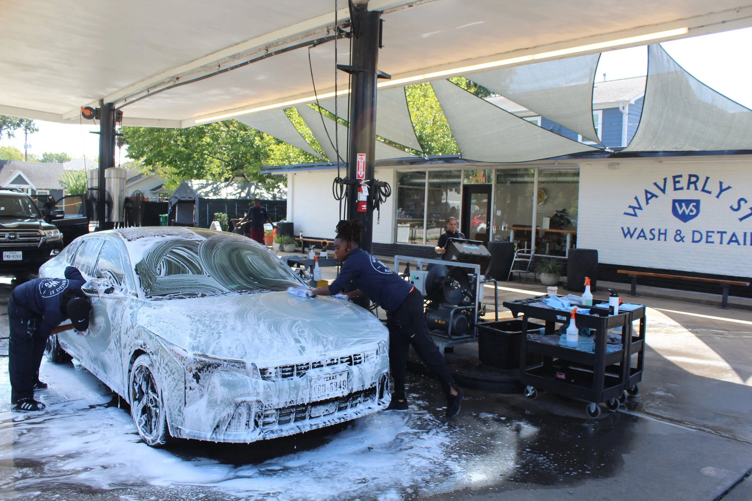 People washing a white car with soap and water outside at a wash and detail shop