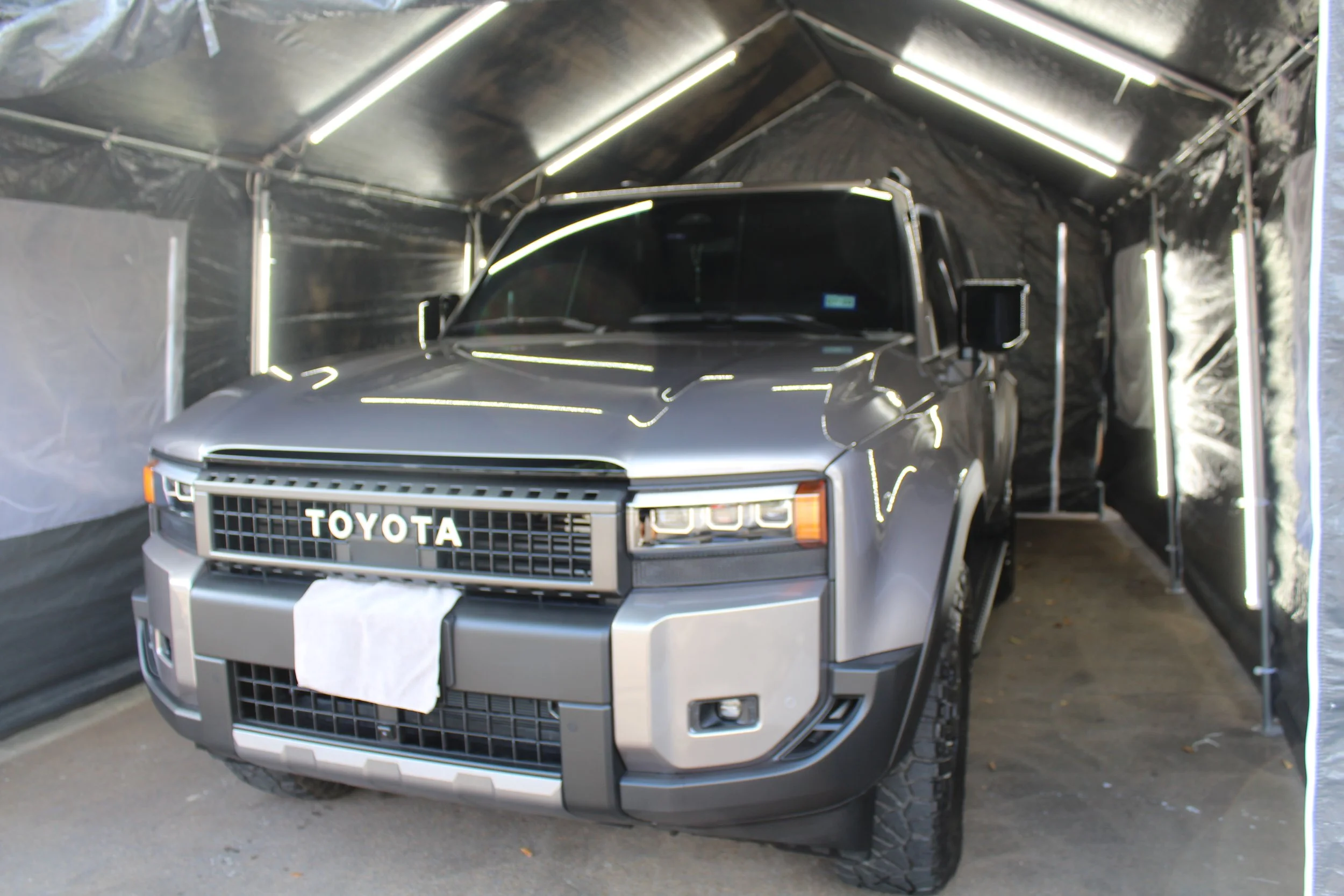A silver Toyota pickup truck parked inside a temporary black fabric enclosure with LED strip lighting.