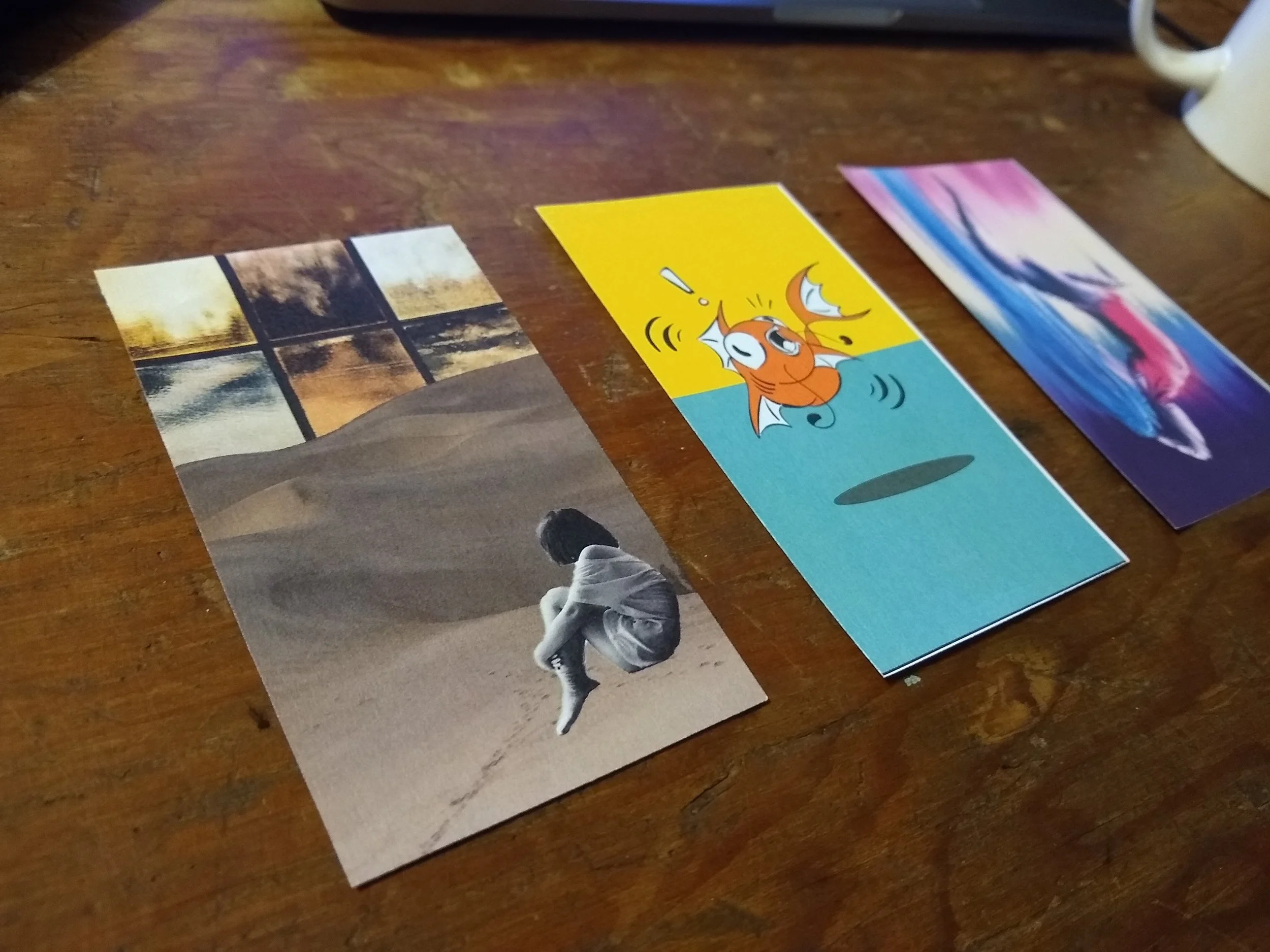Photo of several postcards or photographs spread out on a wooden surface, including a cartoon image of a surprised fox on a bright yellow background.