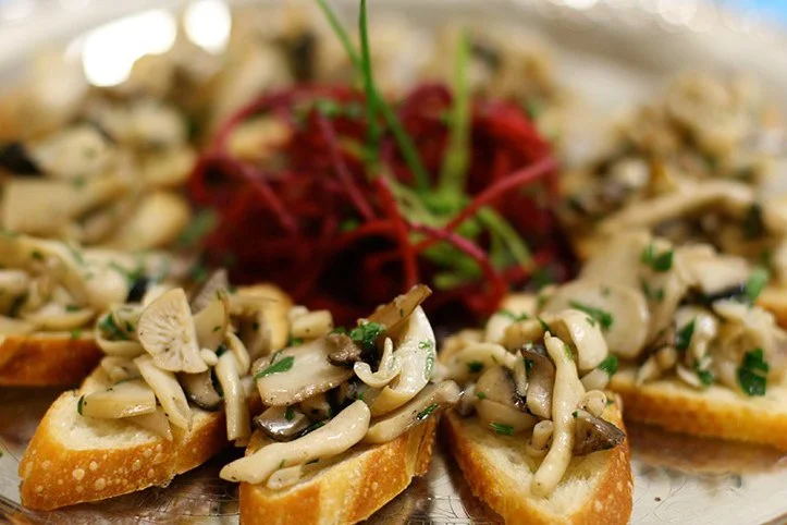 Toasted bread slices topped with a mixture of cooked mushrooms and herbs, garnished with red beets and green herbs.