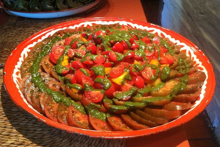 A colorful dish of grilled vegetables topped with chopped tomatoes, bell peppers, and drizzled with green sauce.