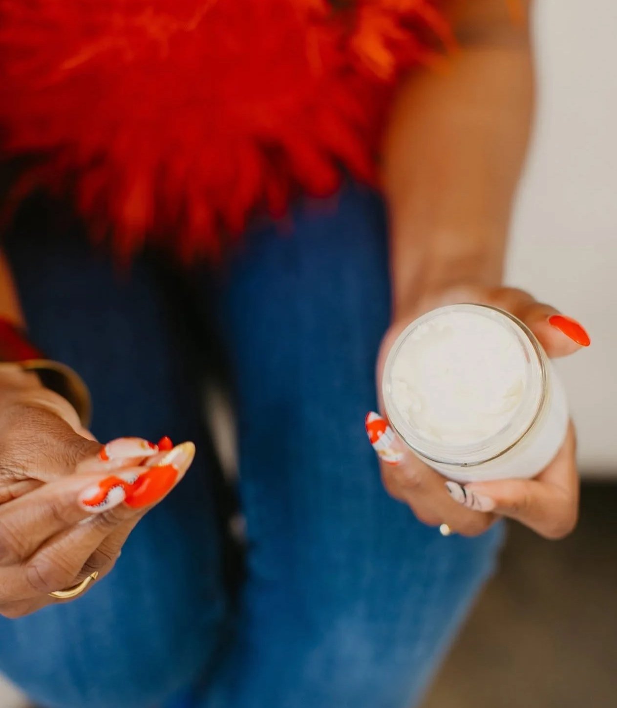 A person with red and white nail polish holding a bottle of white lotion or cream, showing the top view of the container.