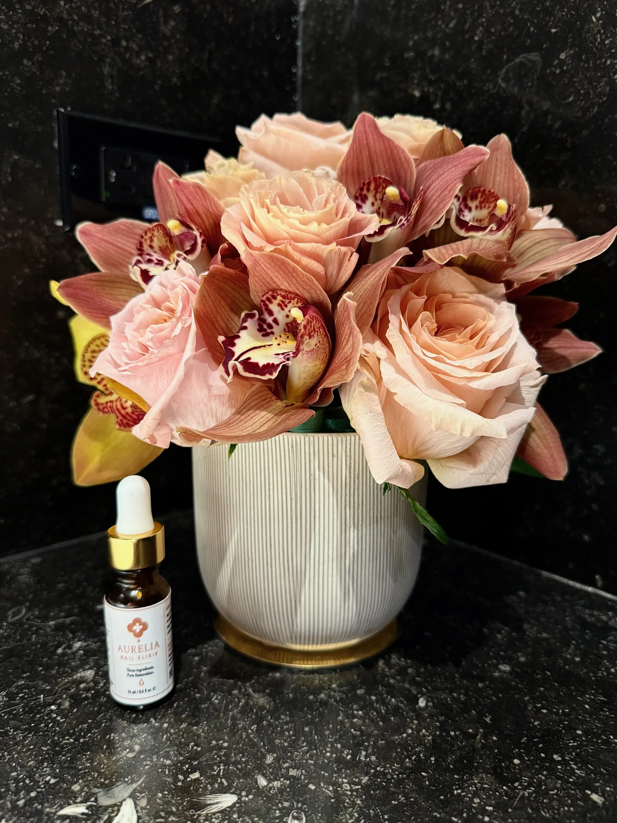Aurelia Nail Elixir bottle styled with fresh flowers, reflecting intentional self-care and natural nail care.