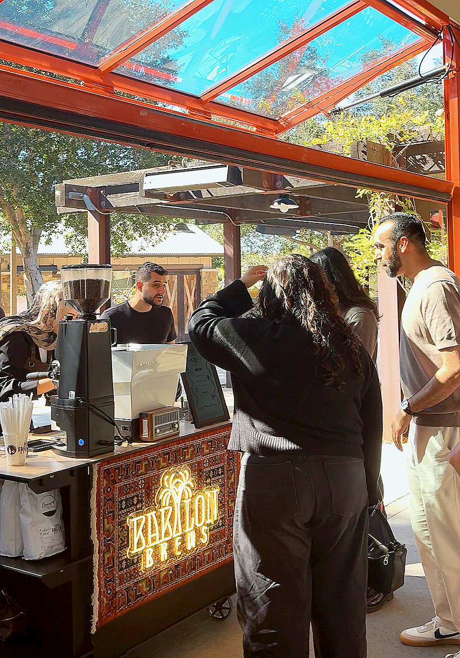 People at a coffee stand with a sign that says 'Zabiont Brews' under a red and glass canopy.