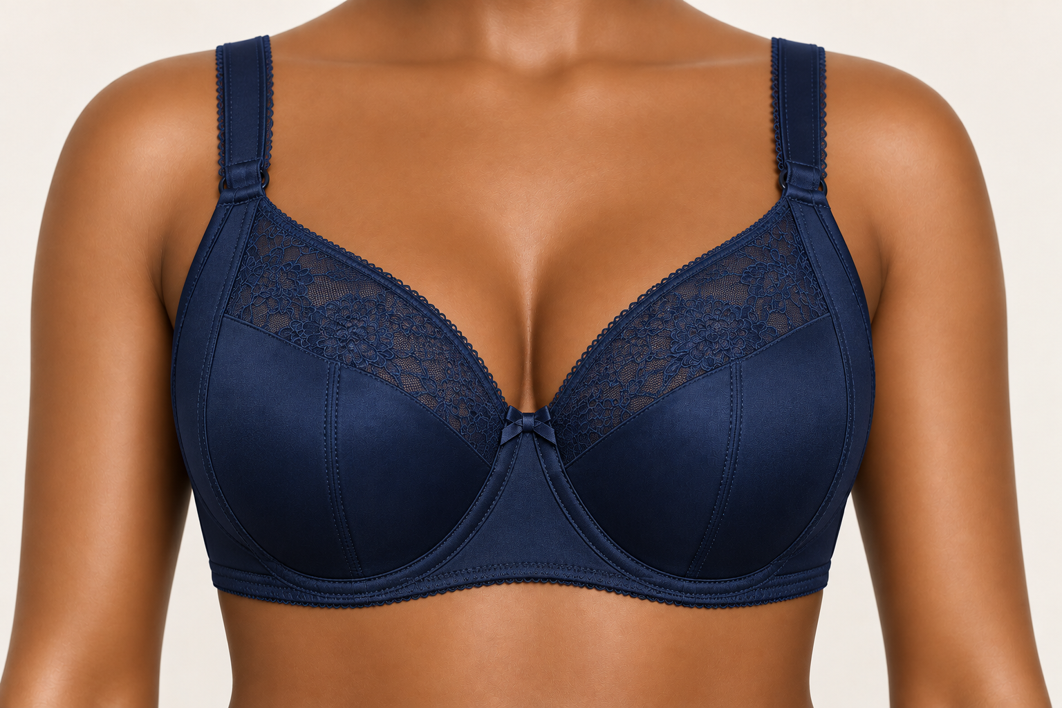 Close-up of a woman wearing a dark blue lace and satin underwire bra with a small bow in the center.