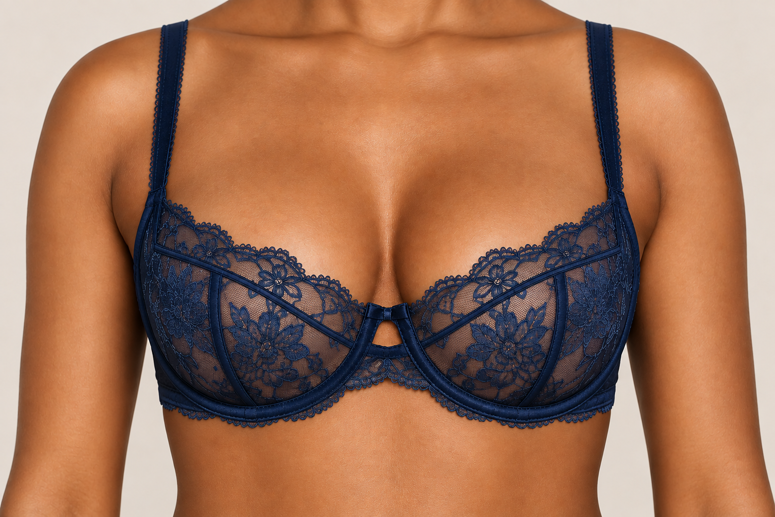 A woman wearing a dark blue lace bra with floral embroidery and satin trim, close-up on upper torso.