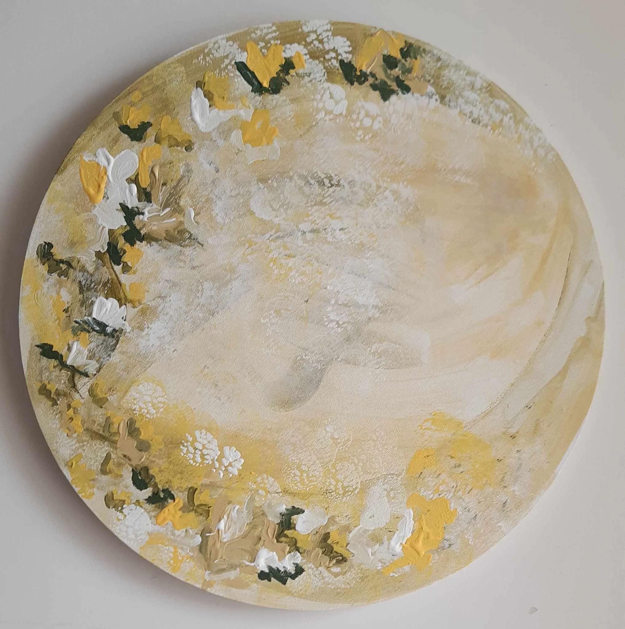 Close-up of a painted surface with yellow, white, black, and green paint splashes and textured brushstrokes on a rounded surface.