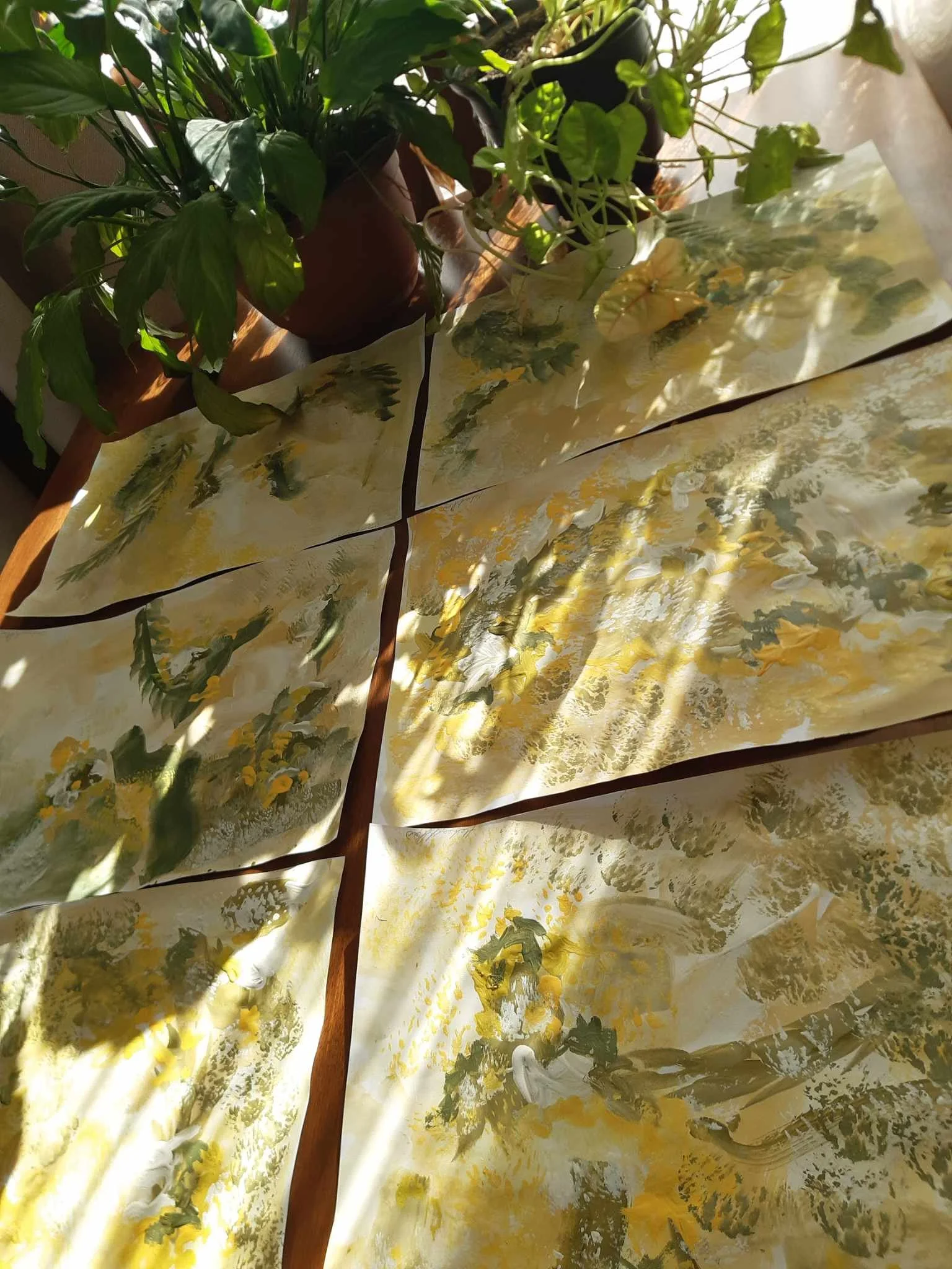 Close-up of a table with plastic tablecloth featuring yellow, green, and beige floral patterns, with potted plants placed on it in sunlight.