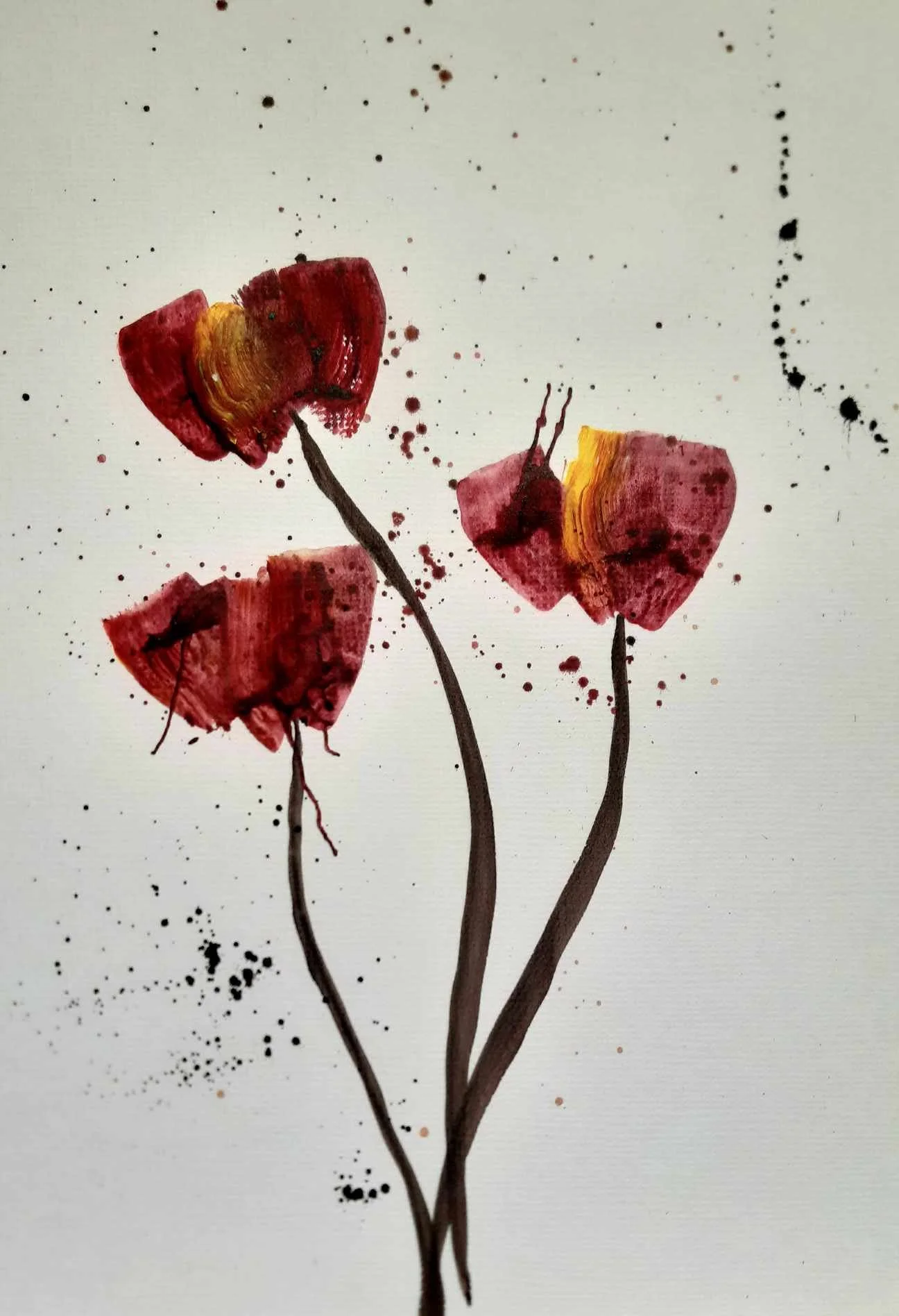 Watercolor painting of three red and yellow poppy flowers with dark stems, splattered black and red paint on a white background.