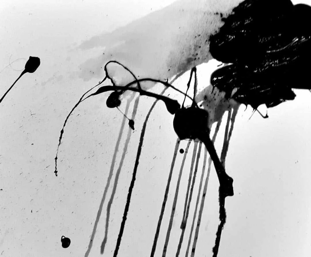 Black ink splattered on white paper creating abstract lines and shapes.