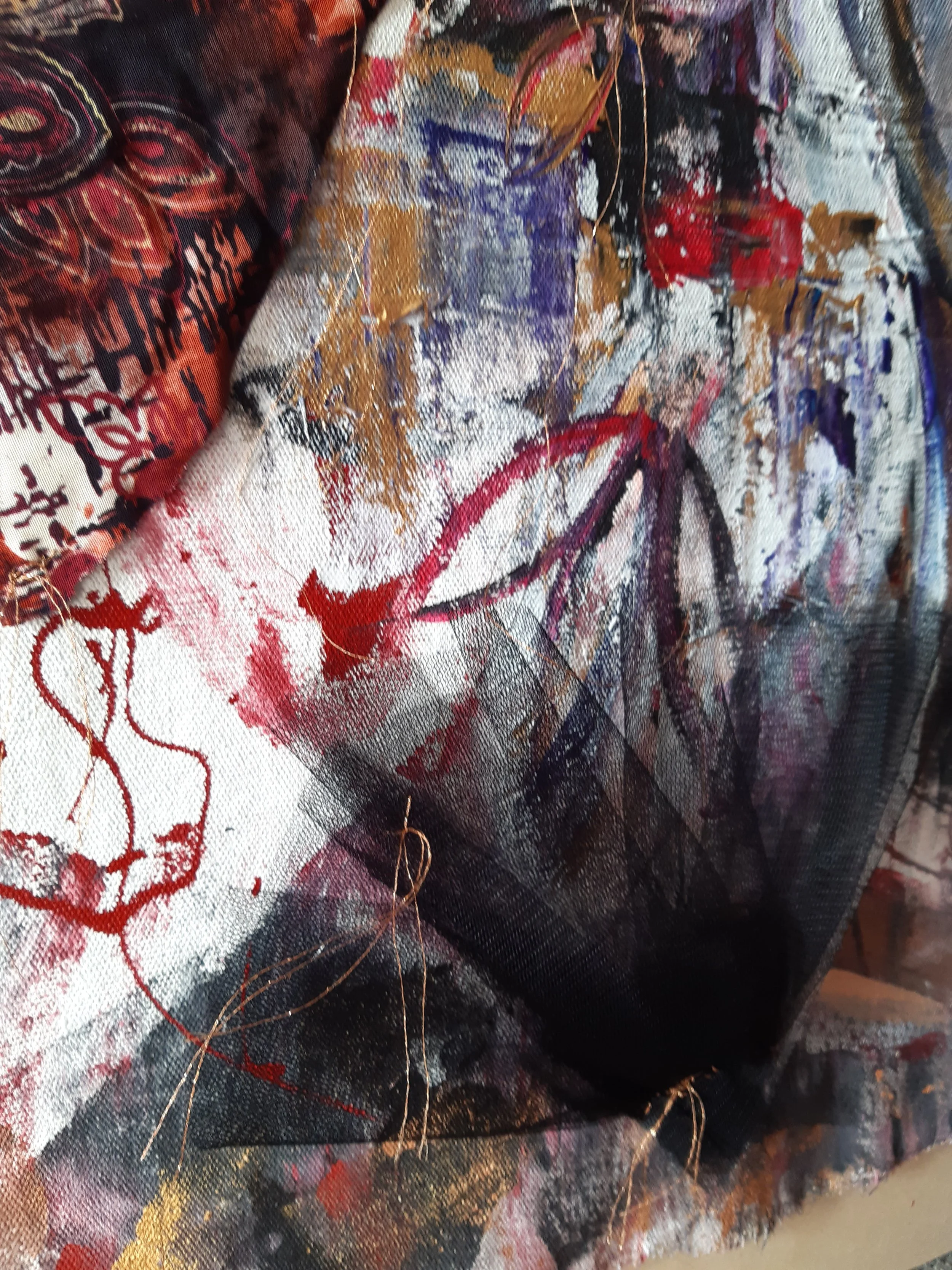 Close-up of abstract, colorful textile artwork with a mix of black, red, white, purple, gold, and blue paint, featuring various patterns, textures, and gold thread accents.