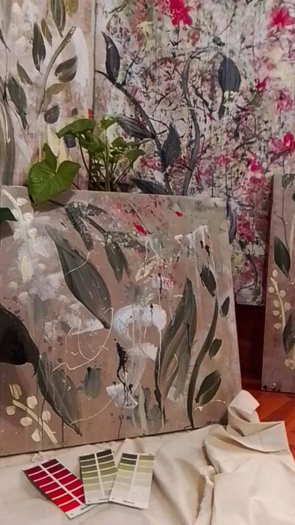 Multiple canvas paintings with abstract botanical designs featuring leaves and flowing paint, along with plant leaves and color swatches.
