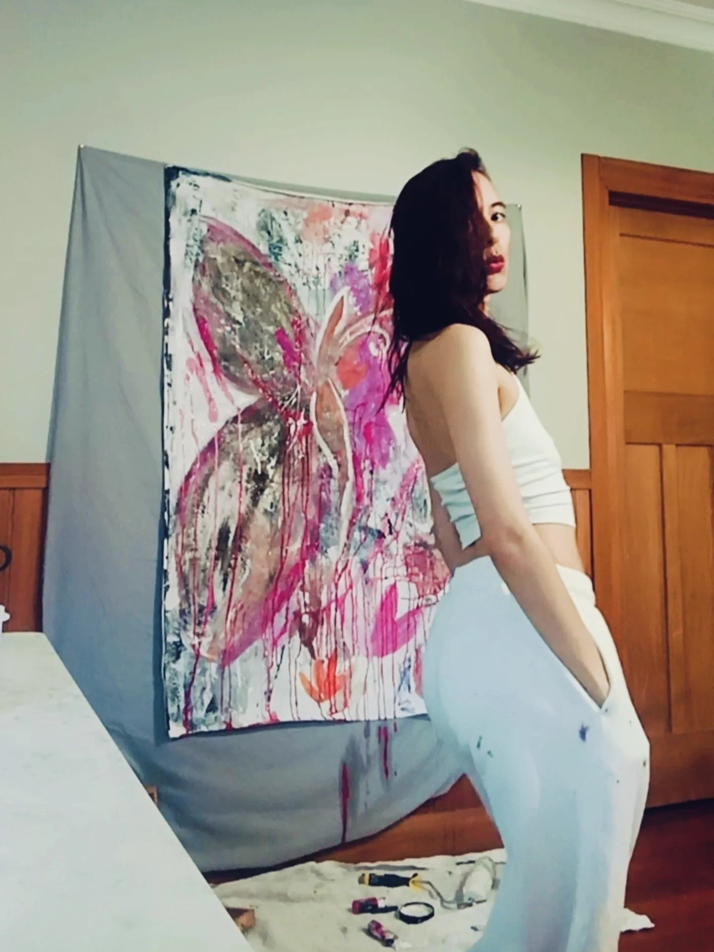 Woman in white dress sitting in front of an abstract painting of a butterfly on canvas.