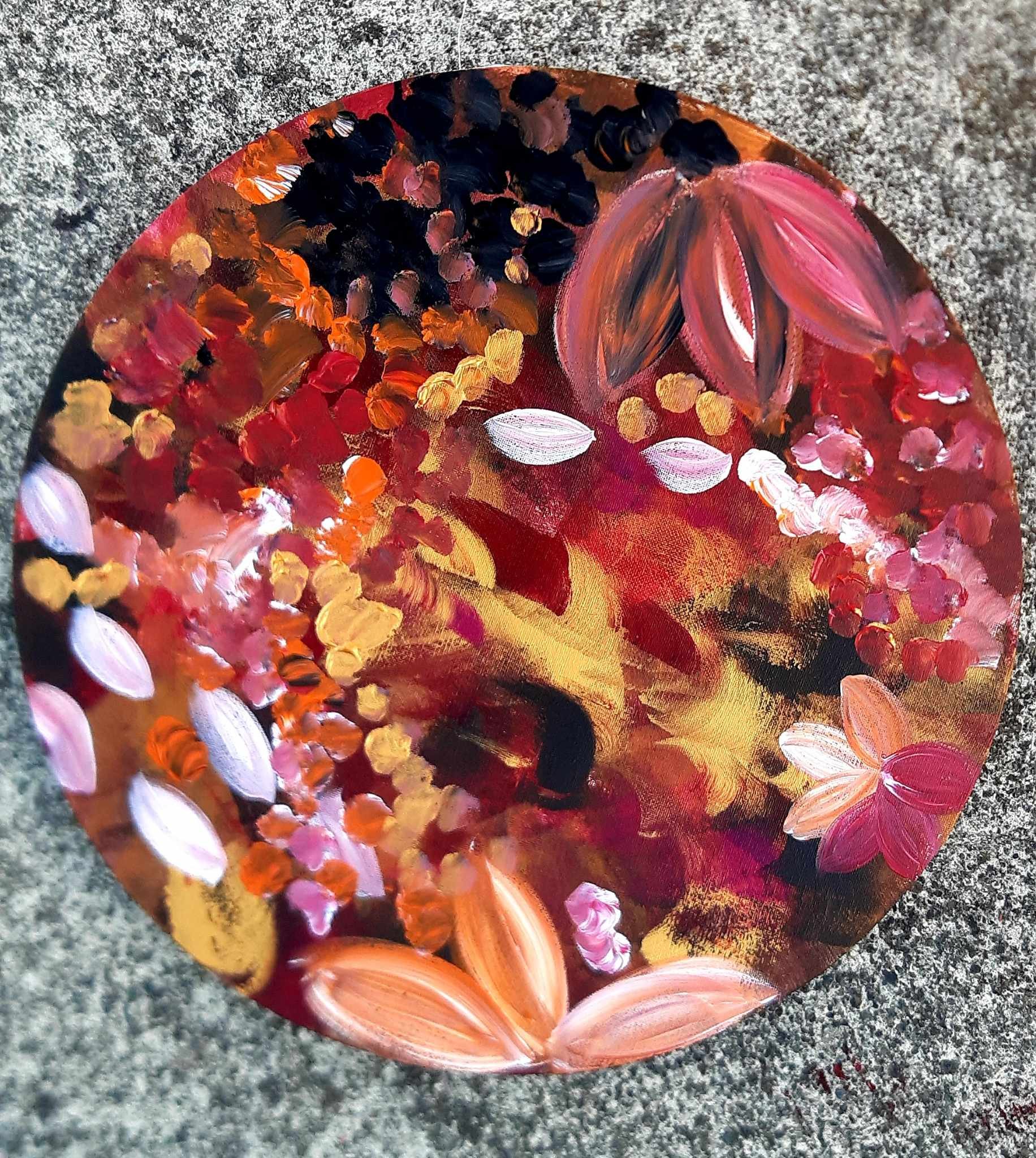 Close-up of an artist's painted decorative rock with abstract orange, pink, and black patterns and floral designs on a gray textured surface.
