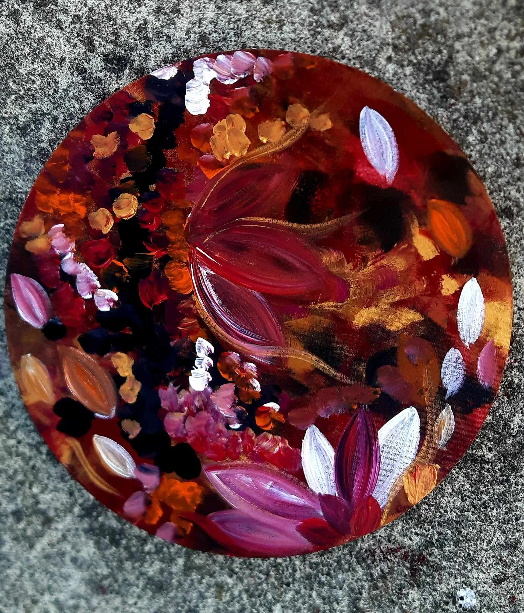 A colorful glass paperweight with swirling red, pink, purple, orange, and black patterns, resting on a textured gray surface.